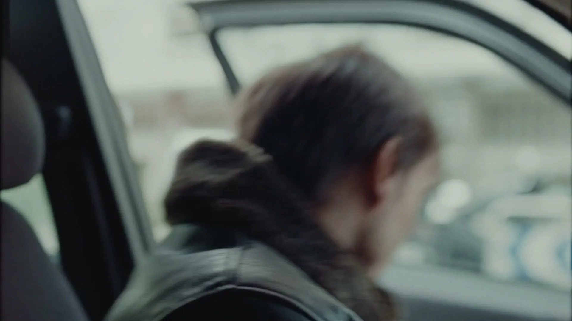 A man and a woman quickly exit a dark green car on a city street, looking around nervously.