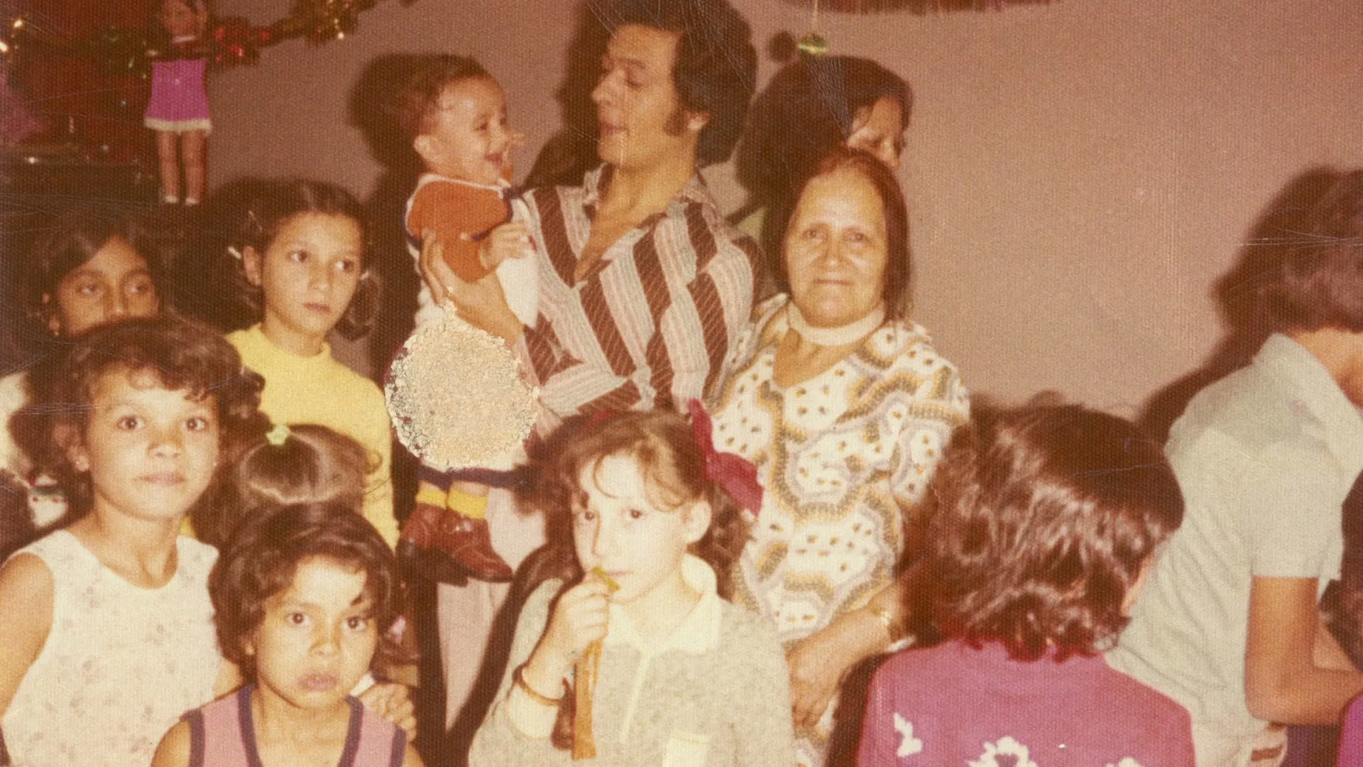 A vintage photo shows a large family gathering, with adults holding babies and children looking at the camera in an interior setting.
