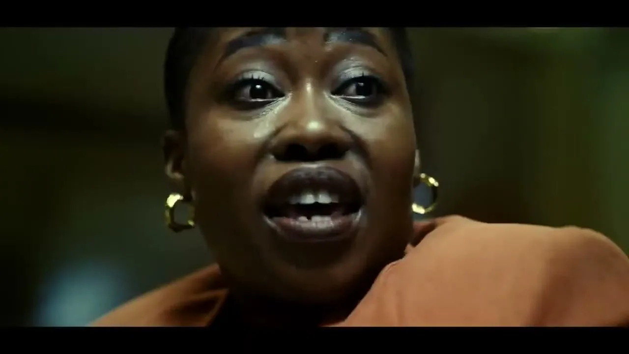 A woman with short hair and gold earrings looks up in fear, then down with a worried expression, in a dimly lit room.