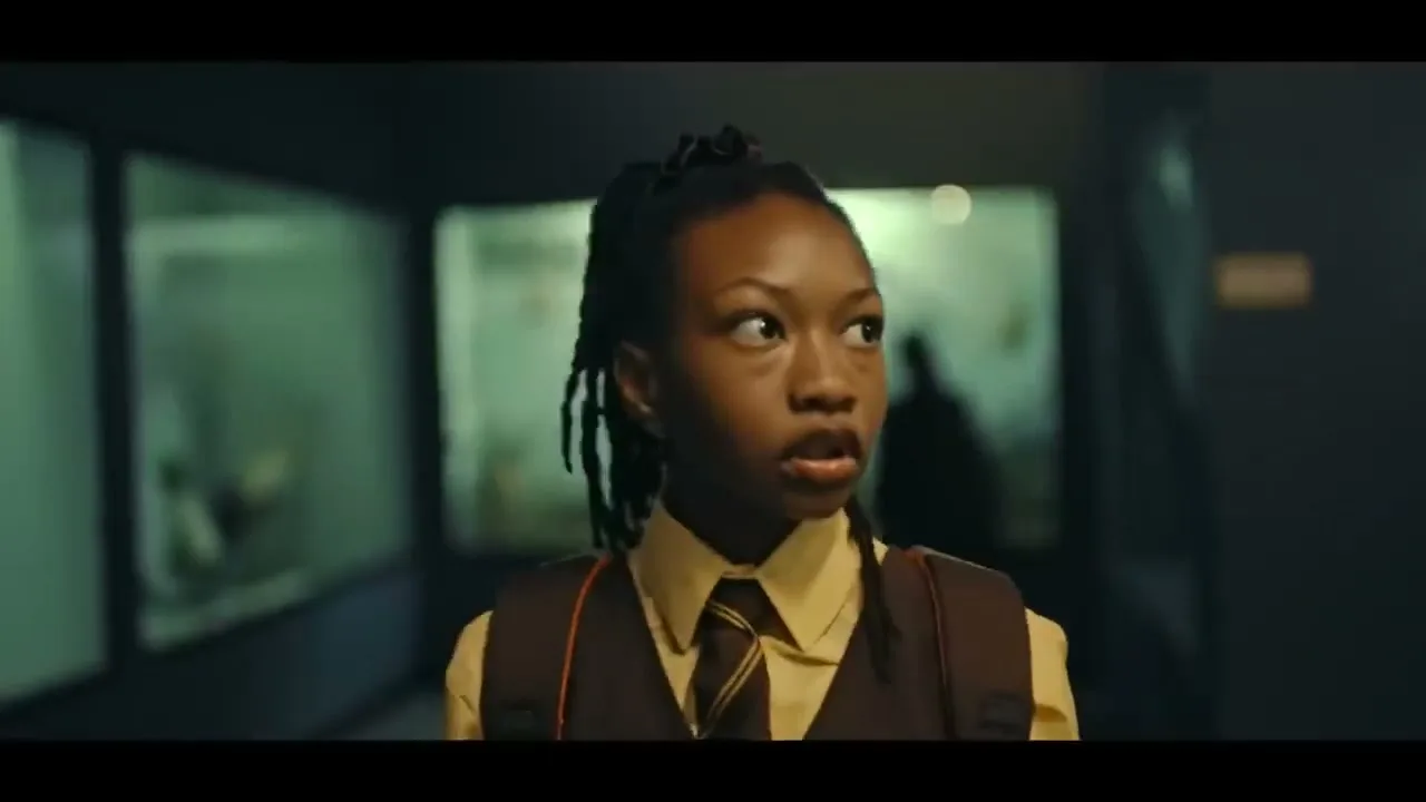 A young Black female student in a school uniform looks around with a scared expression in a dimly lit museum hallway.