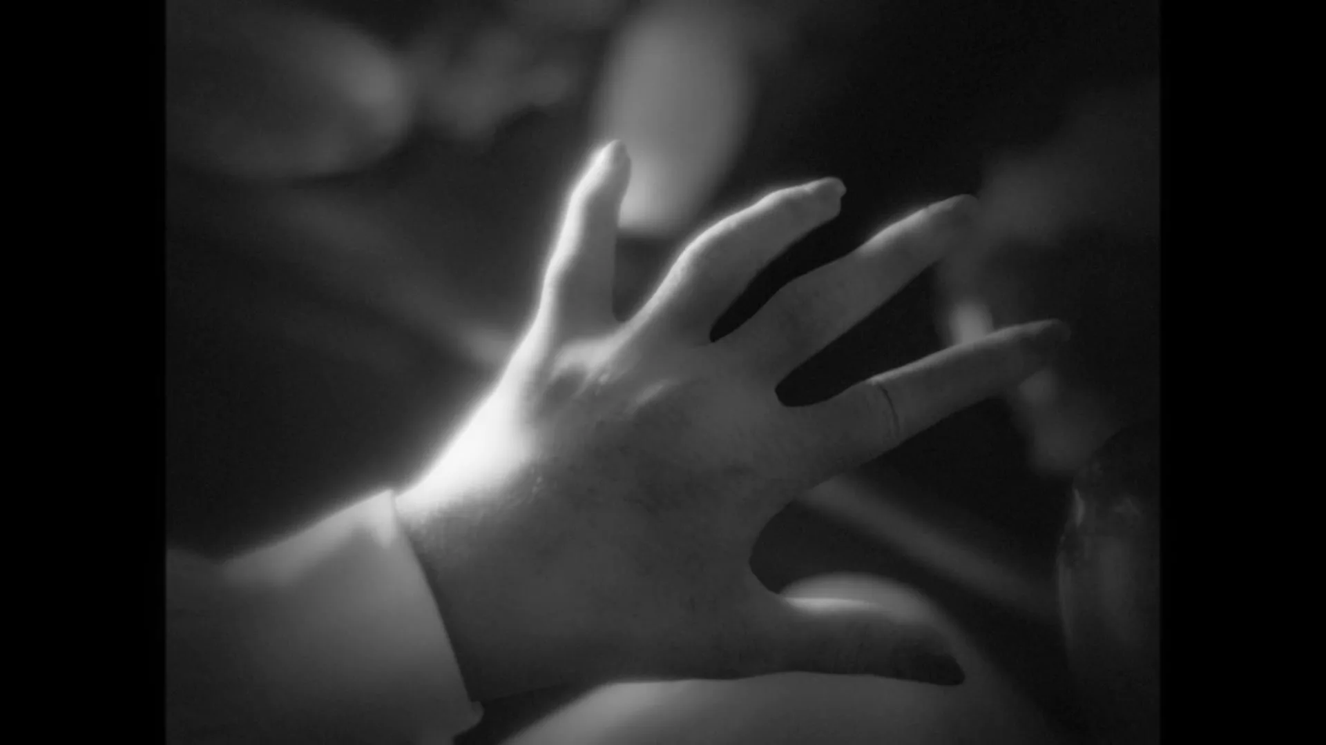 A woman with blonde hair and red lipstick looks down, then a hand reaches out, in a black and white, film noir style.