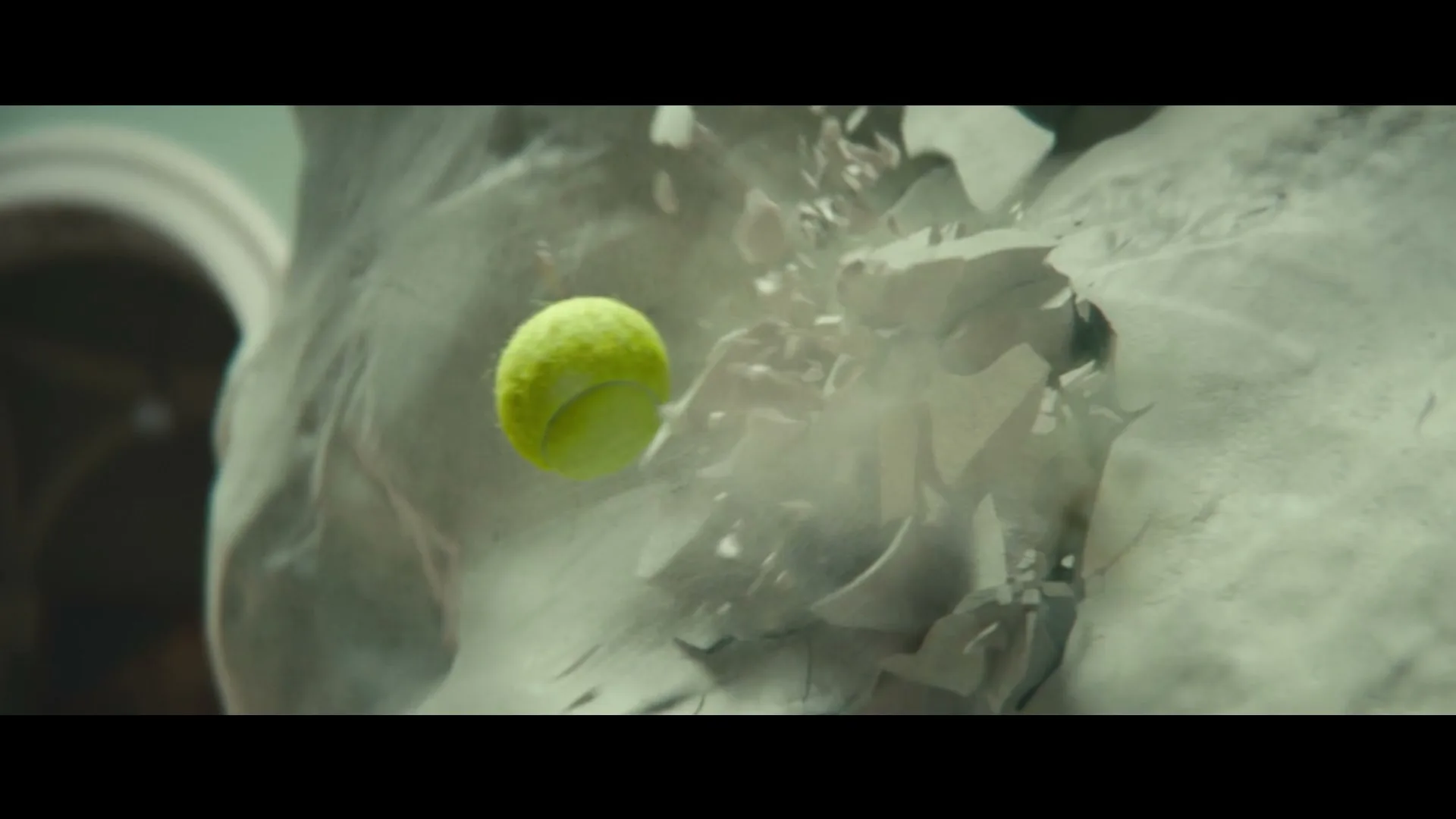A tennis ball hits a white stone statue, causing it to shatter into pieces, in a dramatic slow-motion shot.