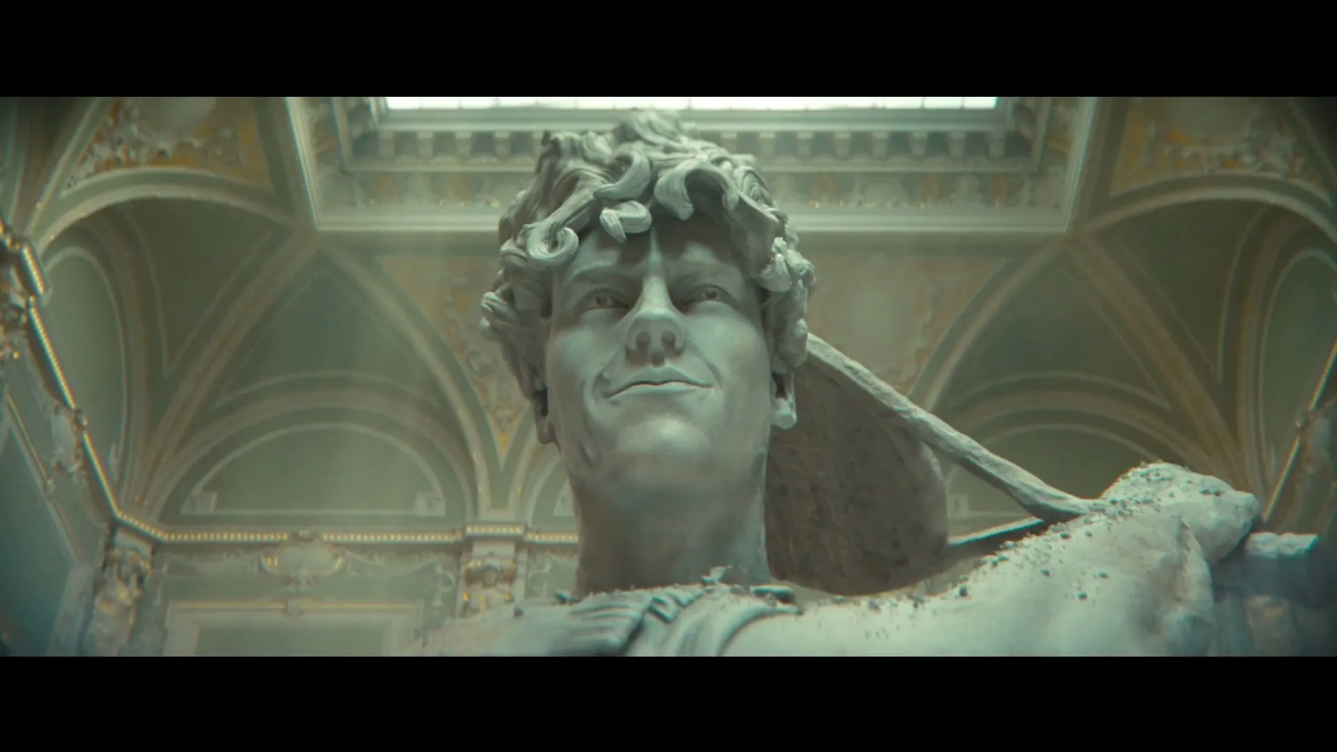 A large, ancient-looking marble statue of a man with curly hair and a slight smile is seen in a grand, ornate hall with a skylight.