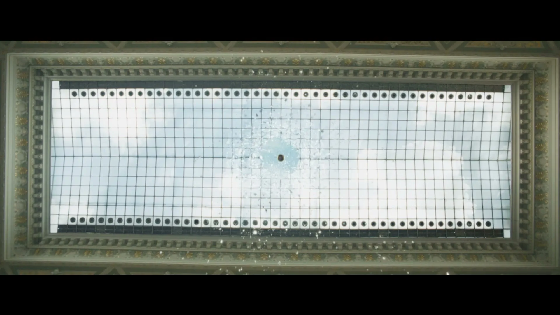 A large, ornate skylight shatters as a brown object falls through it, with pieces of glass flying outwards.