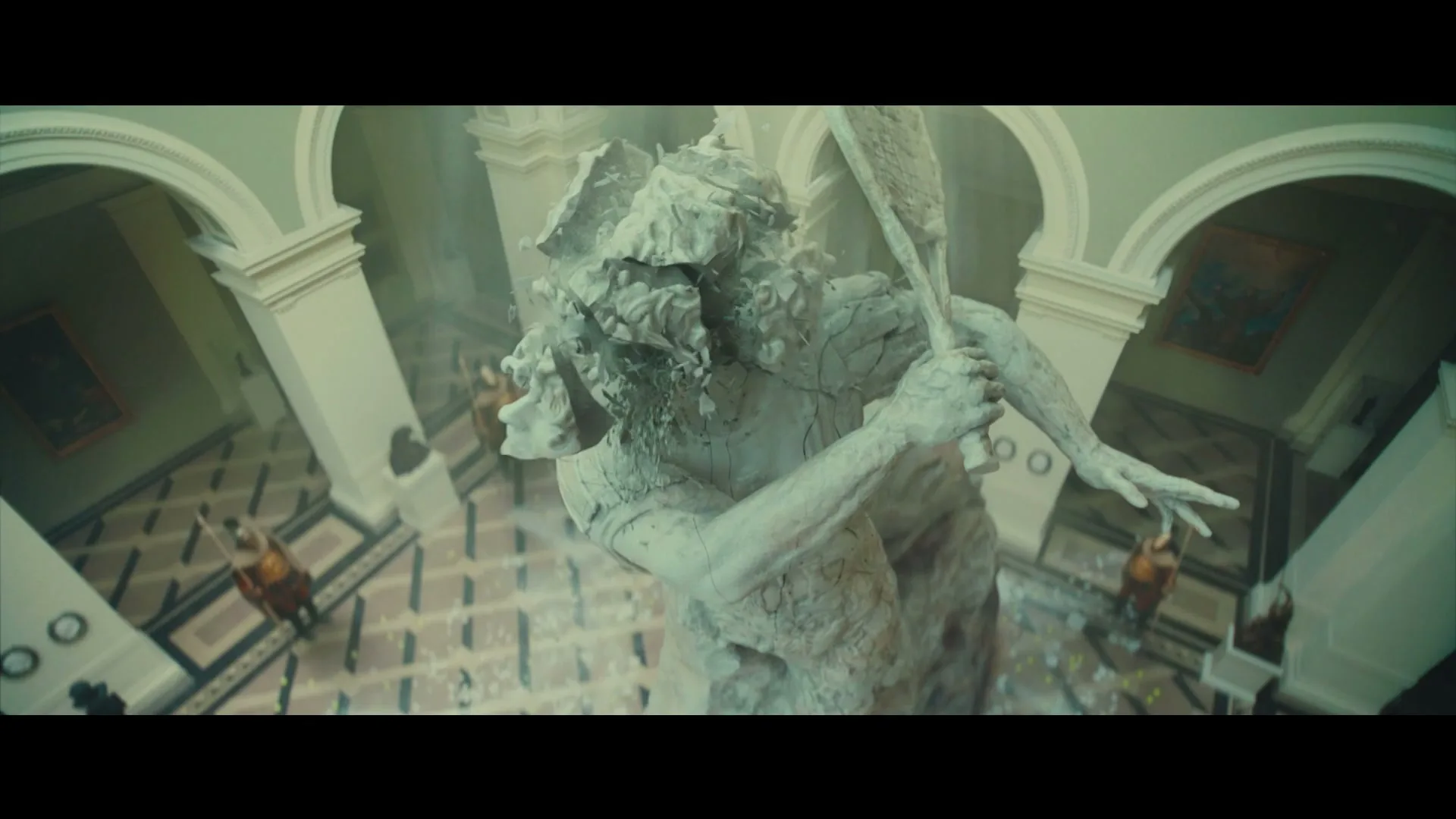 A large, ancient stone statue of a bearded man with a staff crumbles and breaks apart in a grand, ornate hall.