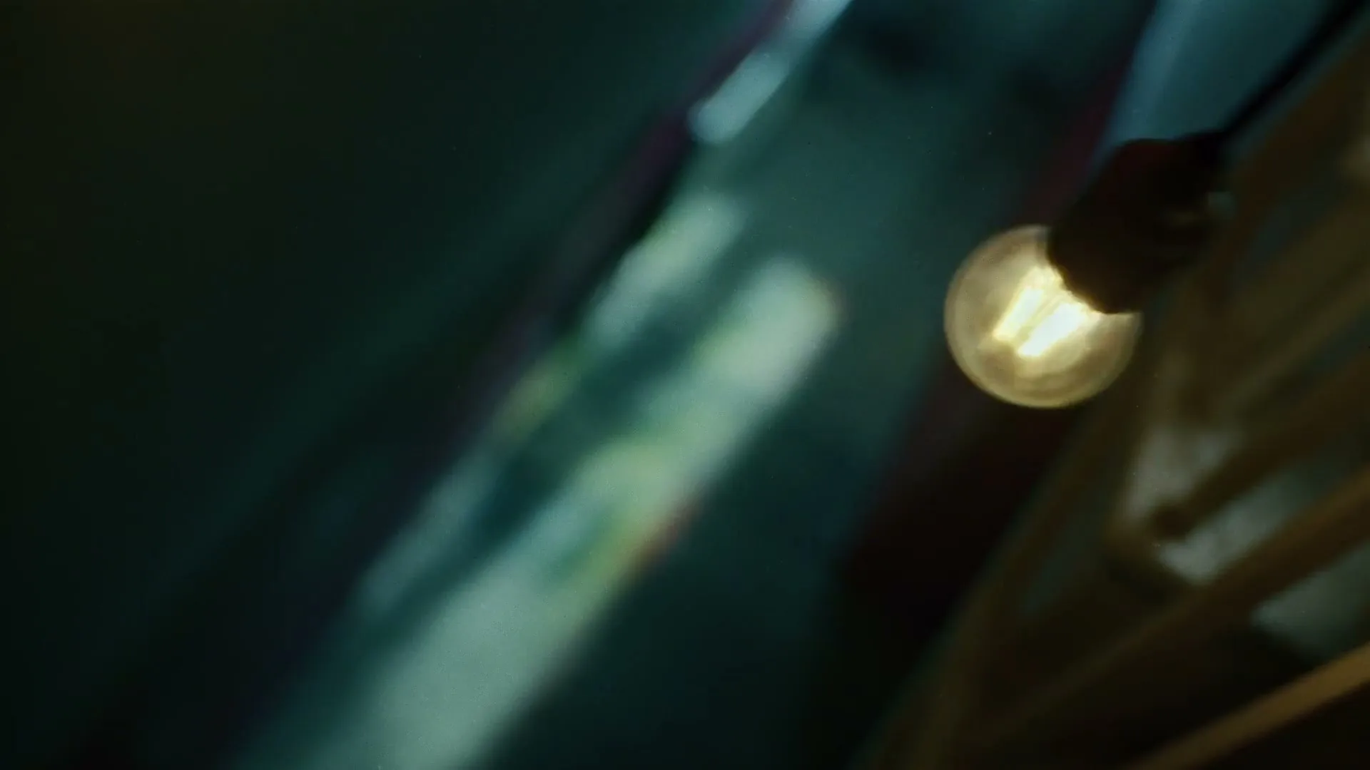 A close-up shot of a glowing lightbulb, hanging from a wire, with a blurry background of what appears to be a room.