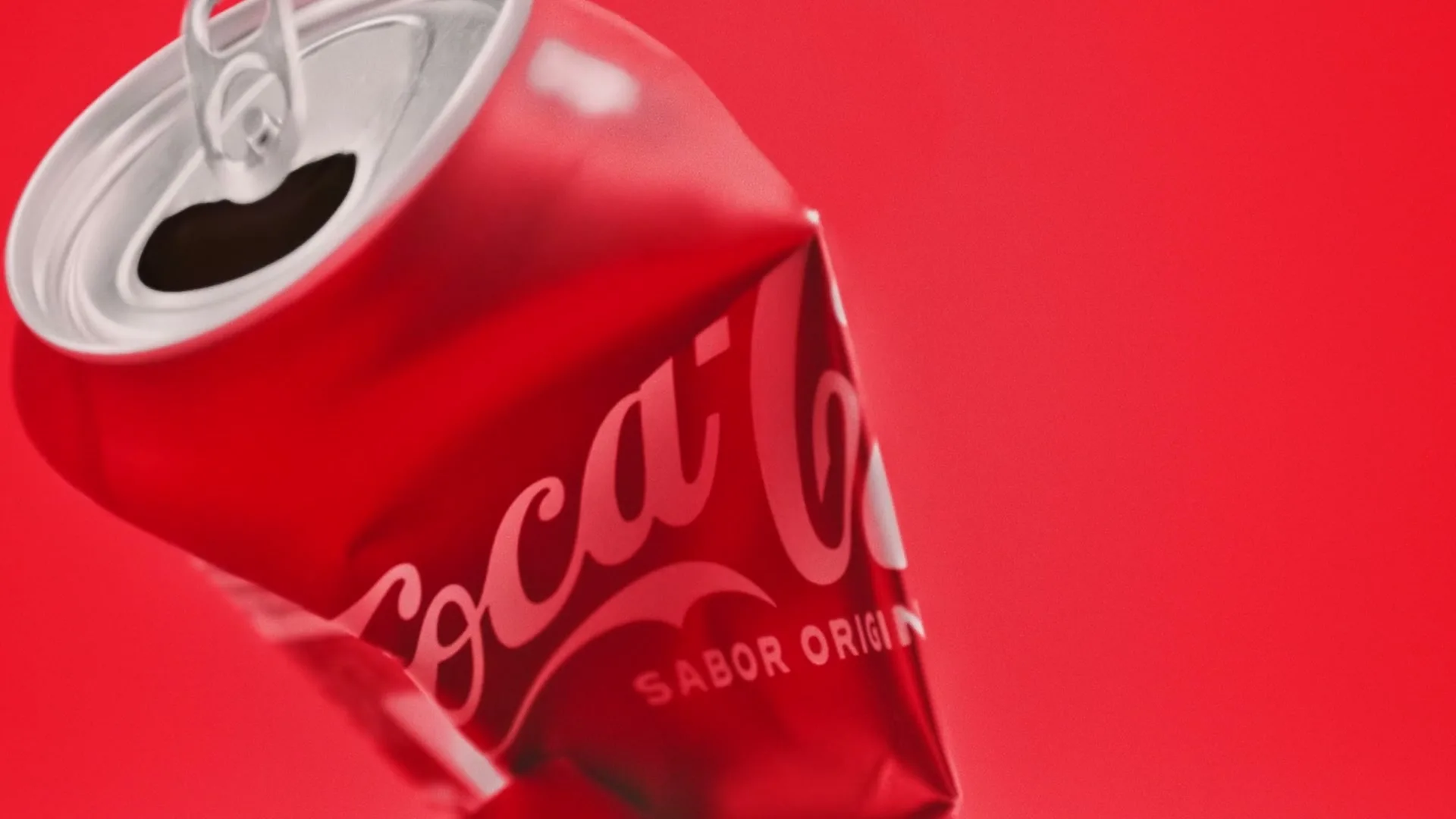A crushed red Coca-Cola can with "SABOR ORIGIN" visible, floats against a solid red background.