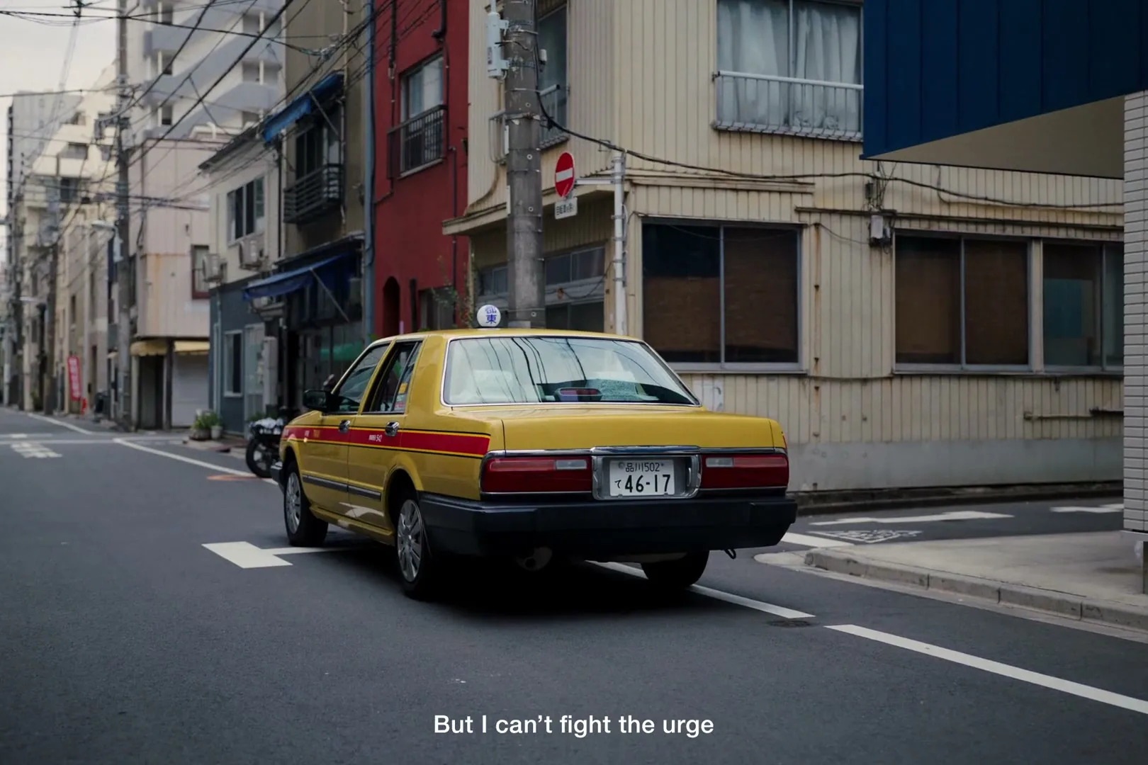 A yellow taxi cab with red stripes drives away from the camera down a narrow street lined with old buildings in a Japanese city.