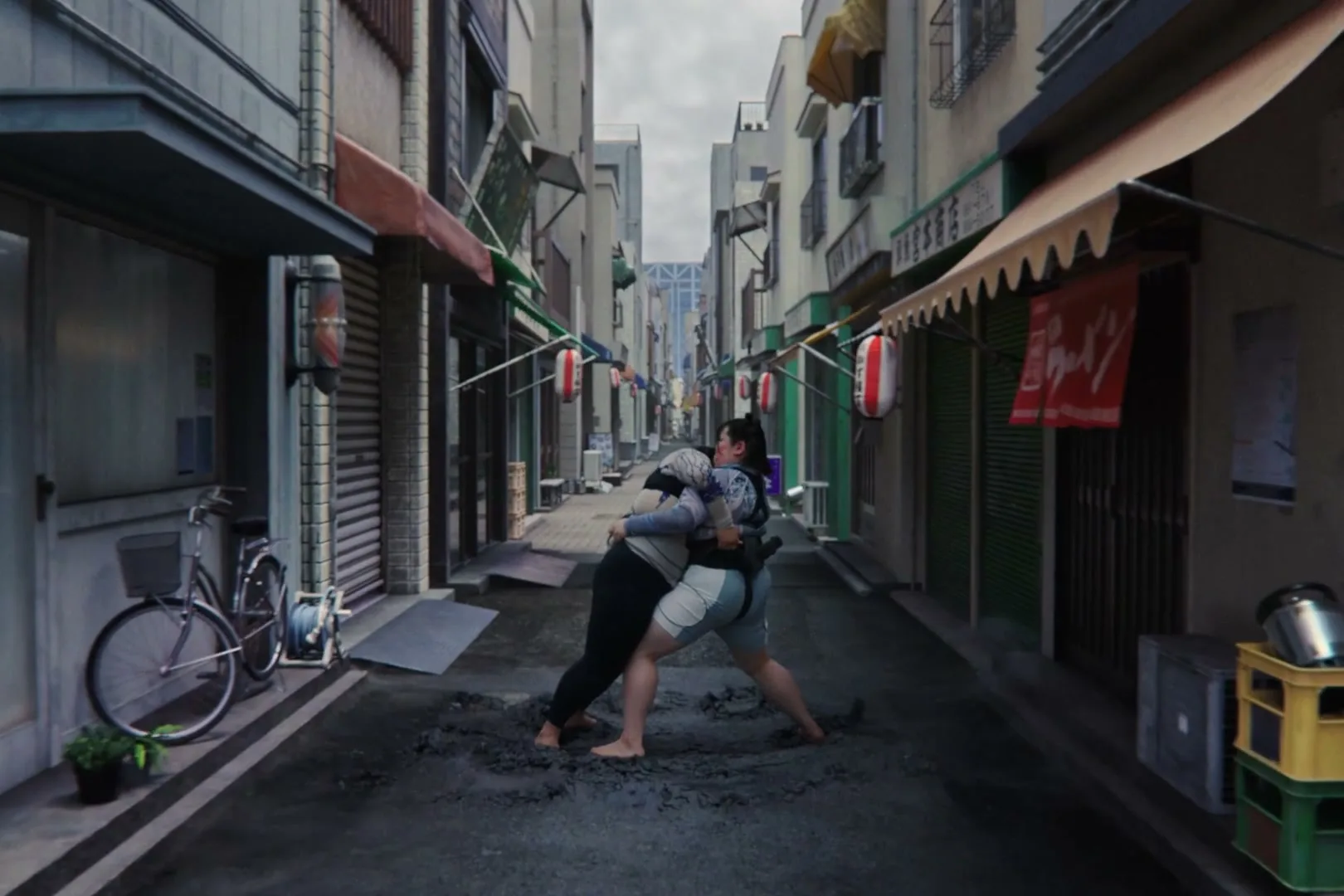 Two women in sumo wrestling attire grapple in a narrow, urban alleyway, surrounded by traditional Japanese buildings under a cloudy sky.