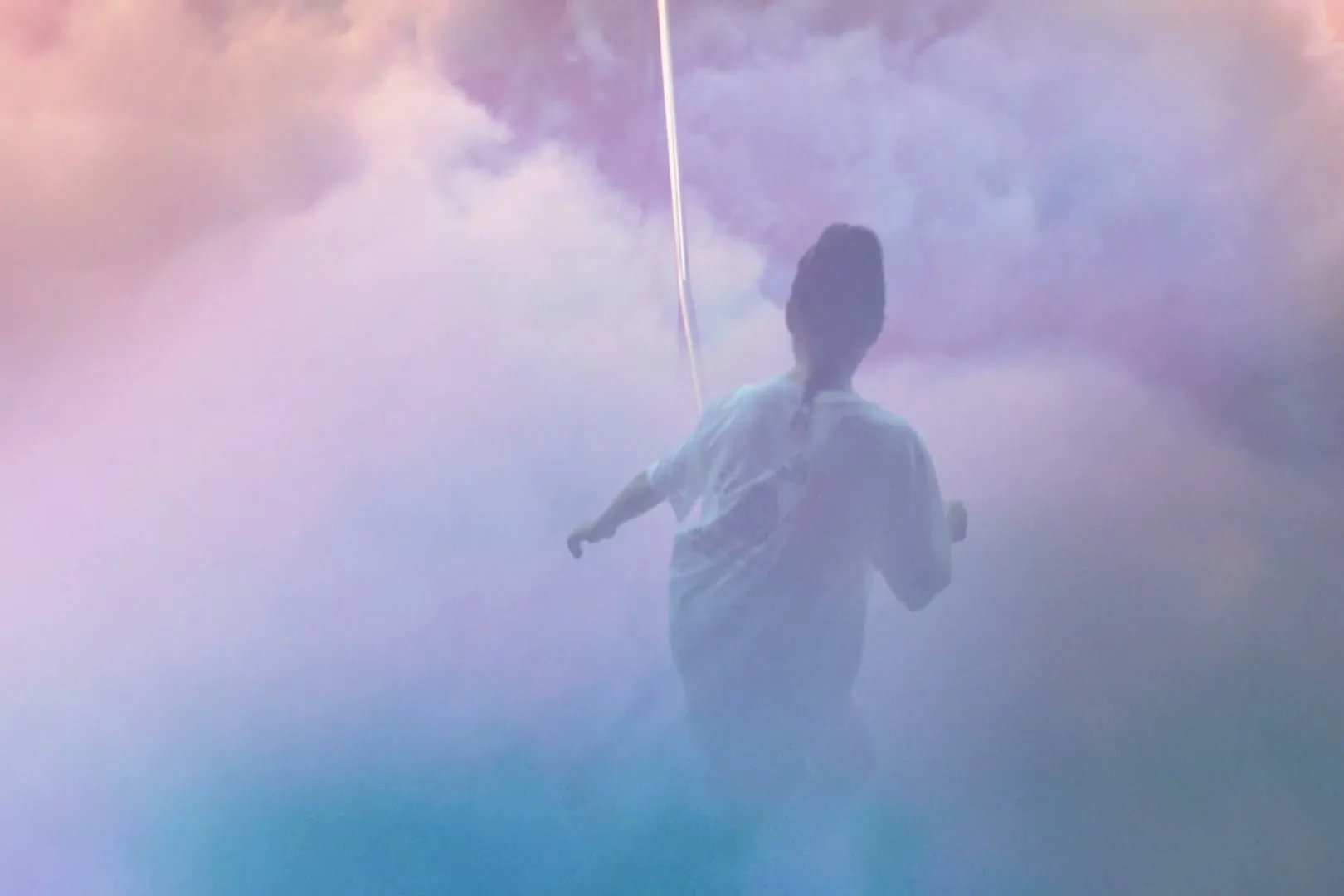 A young woman with a bun in an oversized white t-shirt and teal socks skateboards through colorful clouds in a dreamlike setting.