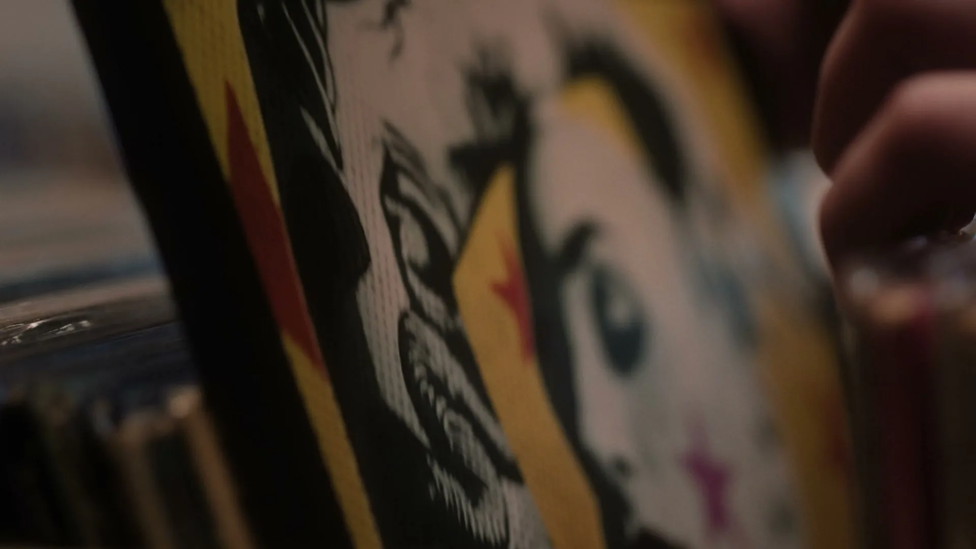A person's hand flips through a collection of vinyl records, revealing colorful album art in a dimly lit interior.