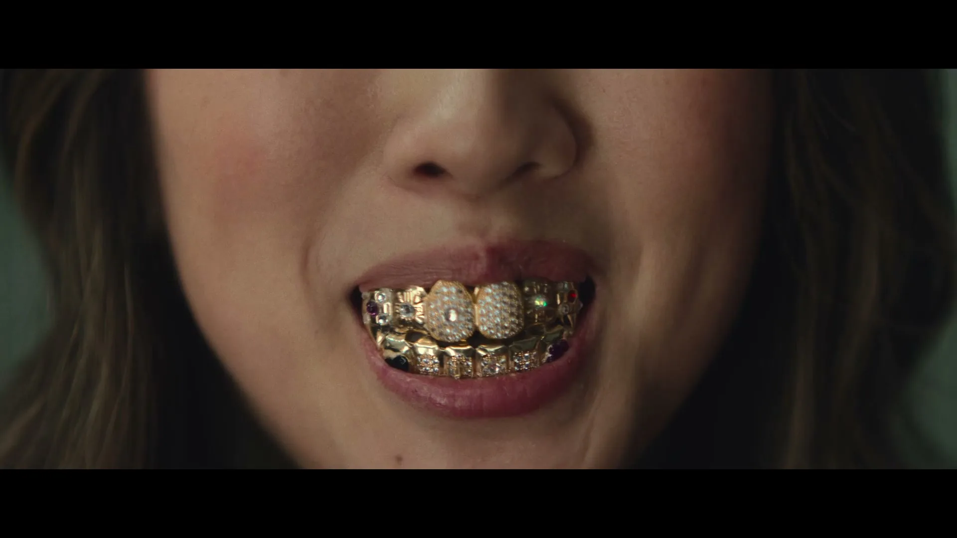 A woman's mouth is shown in a close-up, revealing her gold and diamond grills as she smiles slightly.