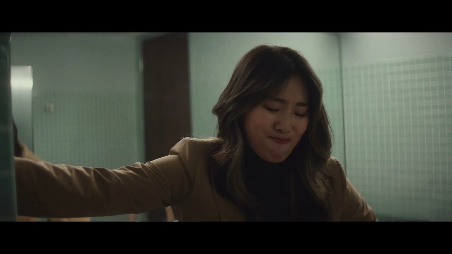 A young Asian woman with long dark hair and gold grills on her teeth looks distressed in a public restroom.