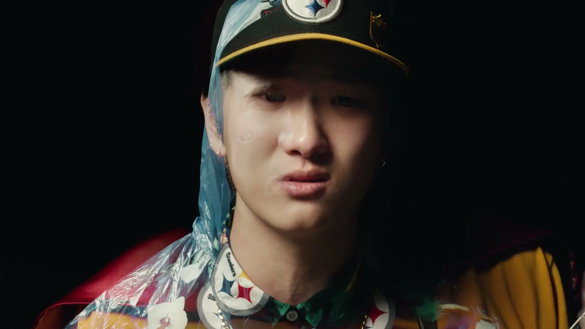 A man with a beard and a baseball cap transforms into a younger man with a different cap and then into a man with a ponytail and a cap, all against a dark background.