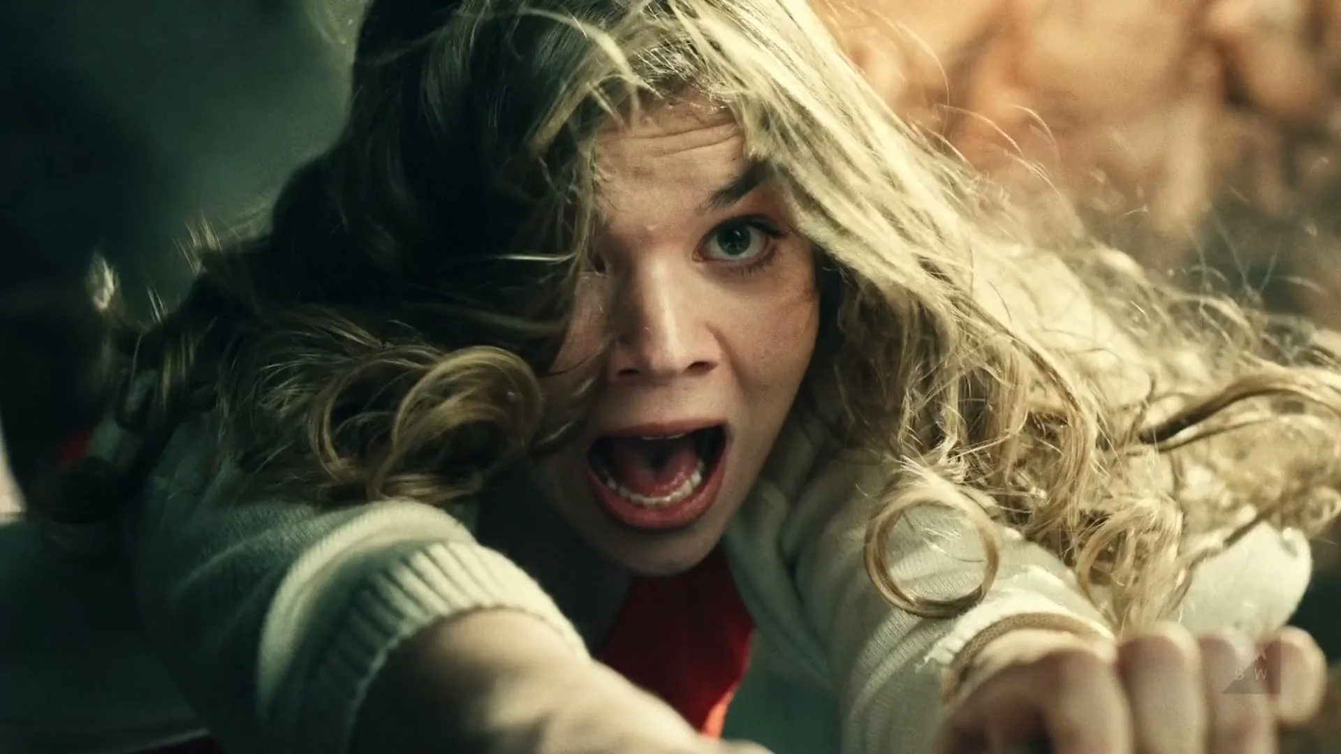 A young woman with blonde hair and a white cardigan screams in terror, reaching out with both hands, in a dark, chaotic setting.