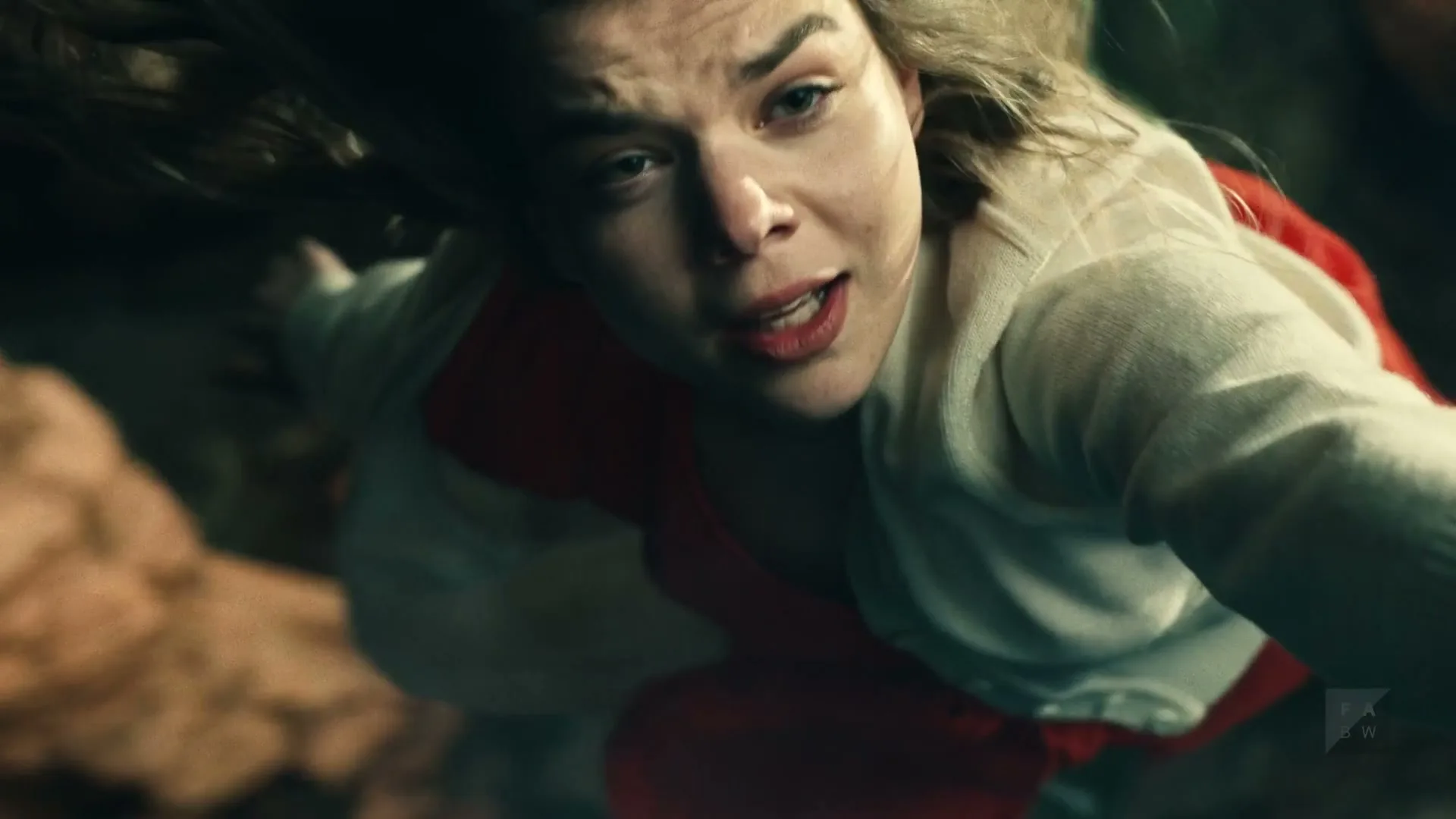 A young woman with blonde hair and a white cardigan falls through a dark, cavernous space, looking up with a terrified expression.
