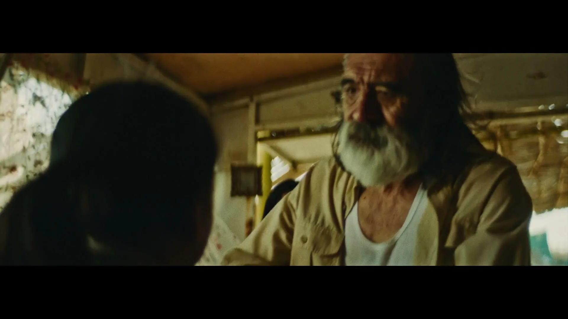 An older man with a white beard and a younger woman stand in a rustic interior, looking at a child whose back is to the camera.