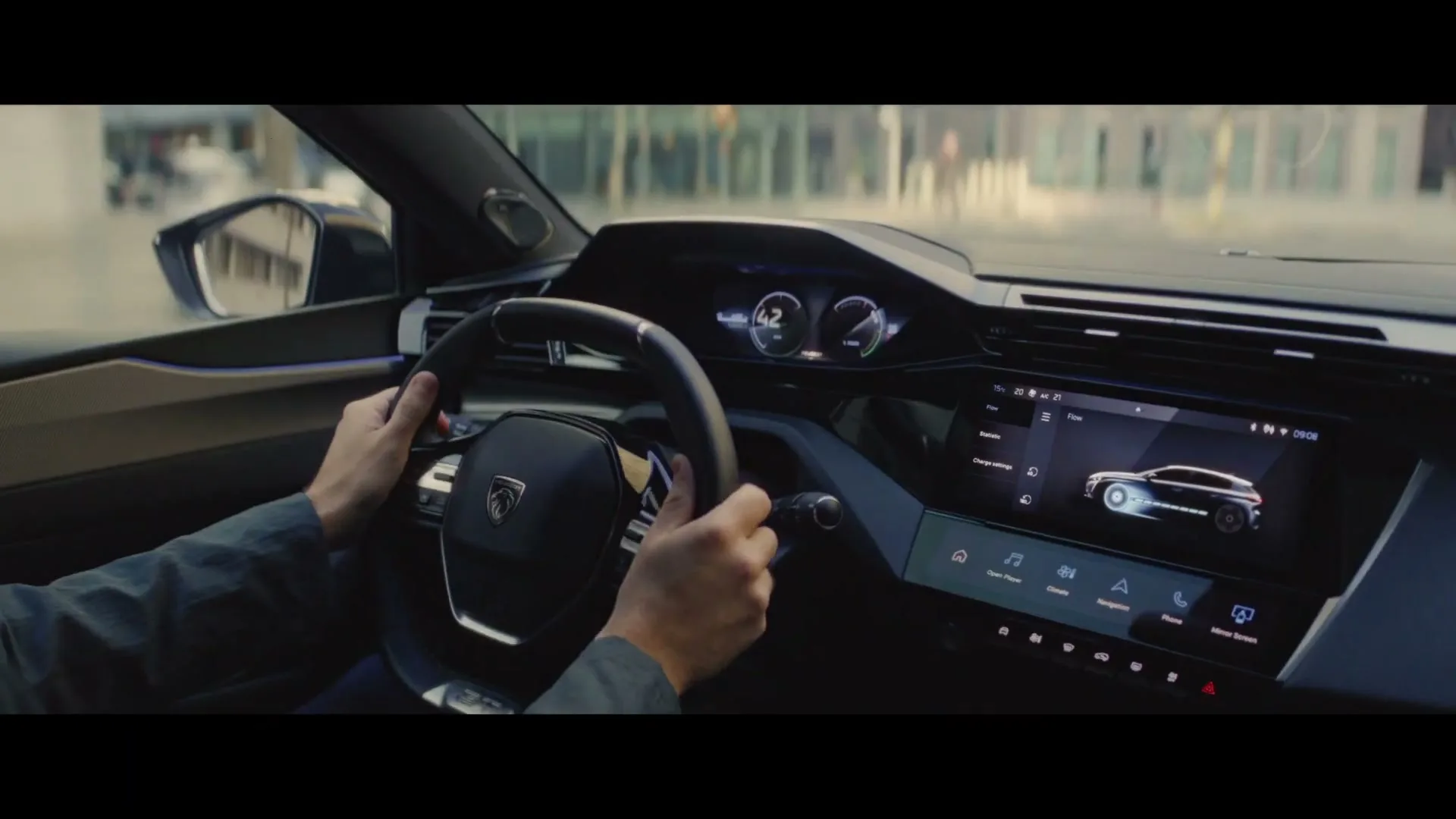 A man's hands are on the steering wheel of a Peugeot car, driving through a city street during the day.