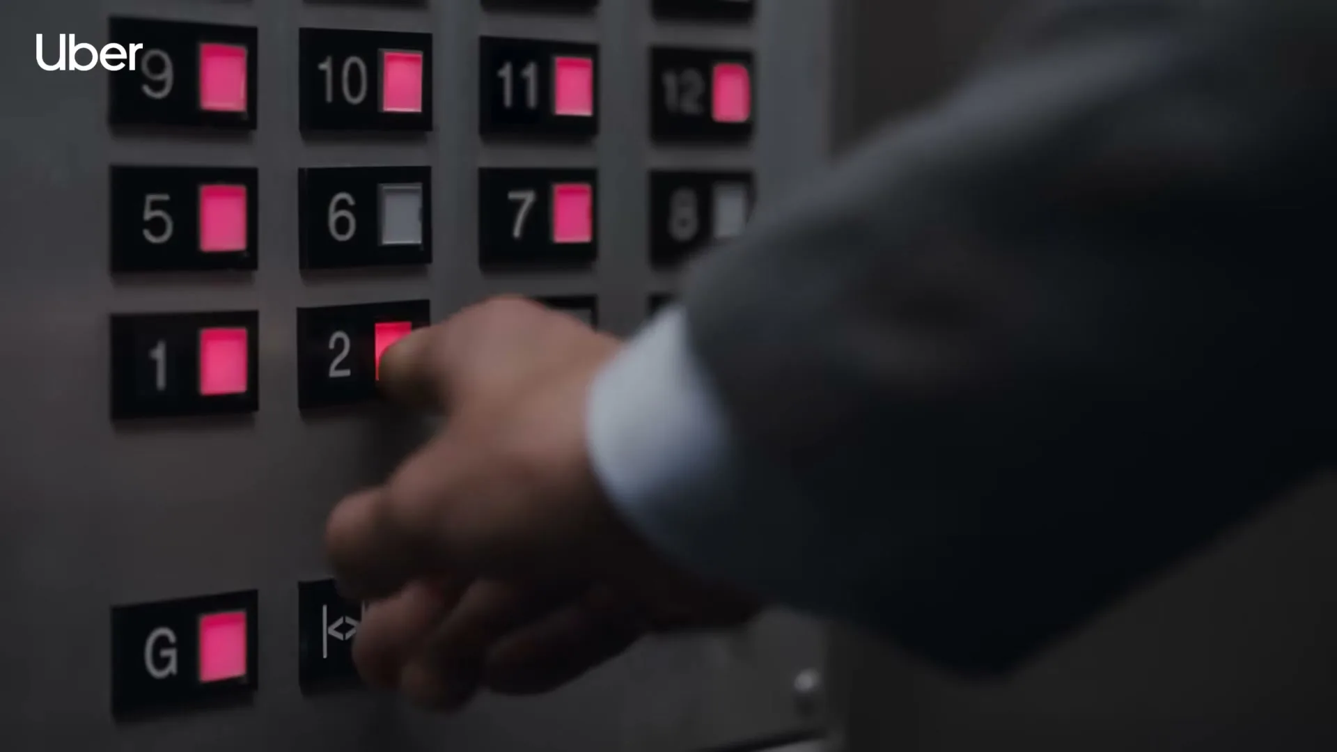 A man in a suit presses the number 2 button on an elevator panel, with other buttons lit up in red.