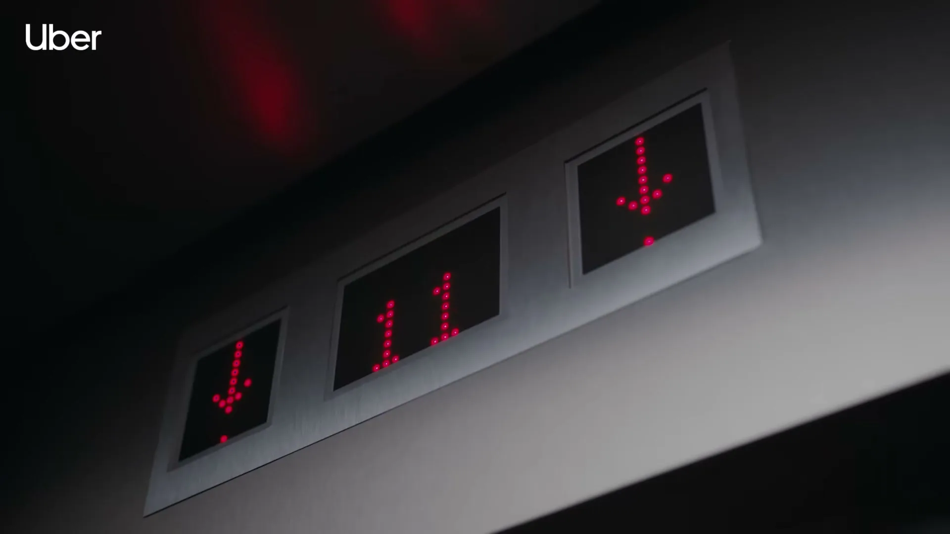 A close-up shot of an elevator panel with red digital numbers and arrows indicating the elevator is on the 11th floor and moving down.