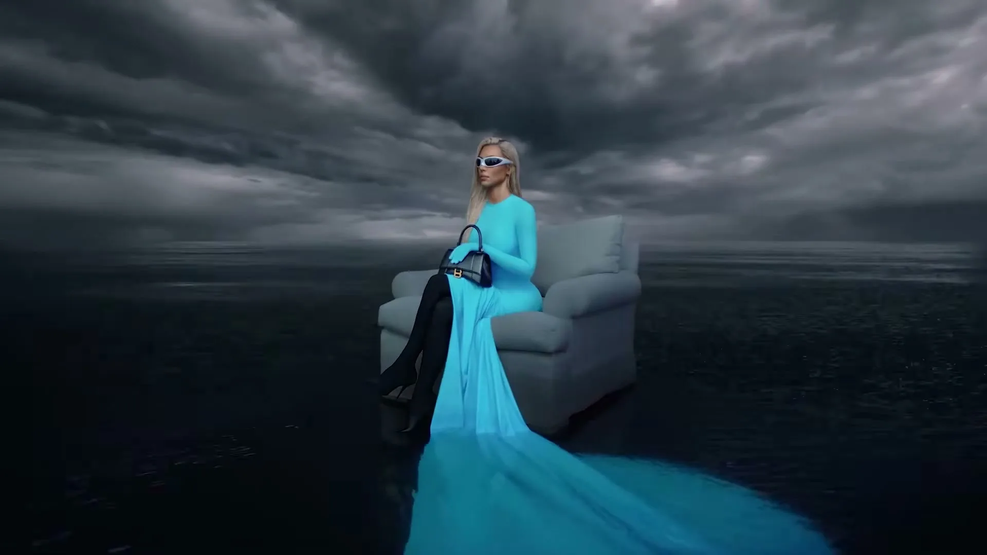A blonde woman in a long blue dress and sunglasses sits on a couch in a dark, stormy, watery landscape, holding a black handbag.