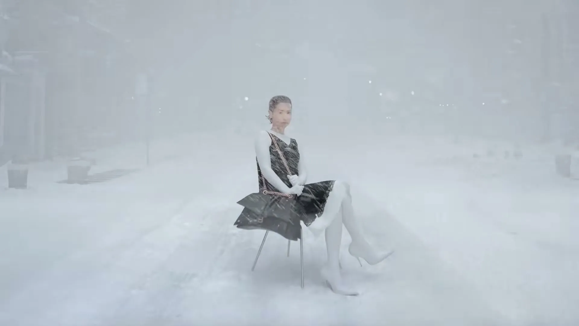 A young woman in a black dress and white boots sits on a chair in a snowy, desolate urban landscape, looking directly at the camera.