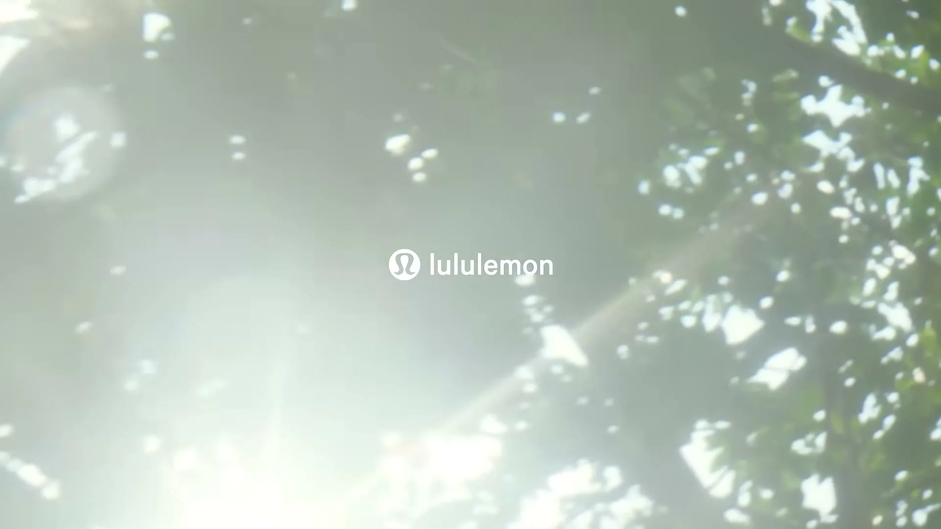 The Lululemon logo and wordmark are visible on screen, with bright sunlight and green leaves in the background.
