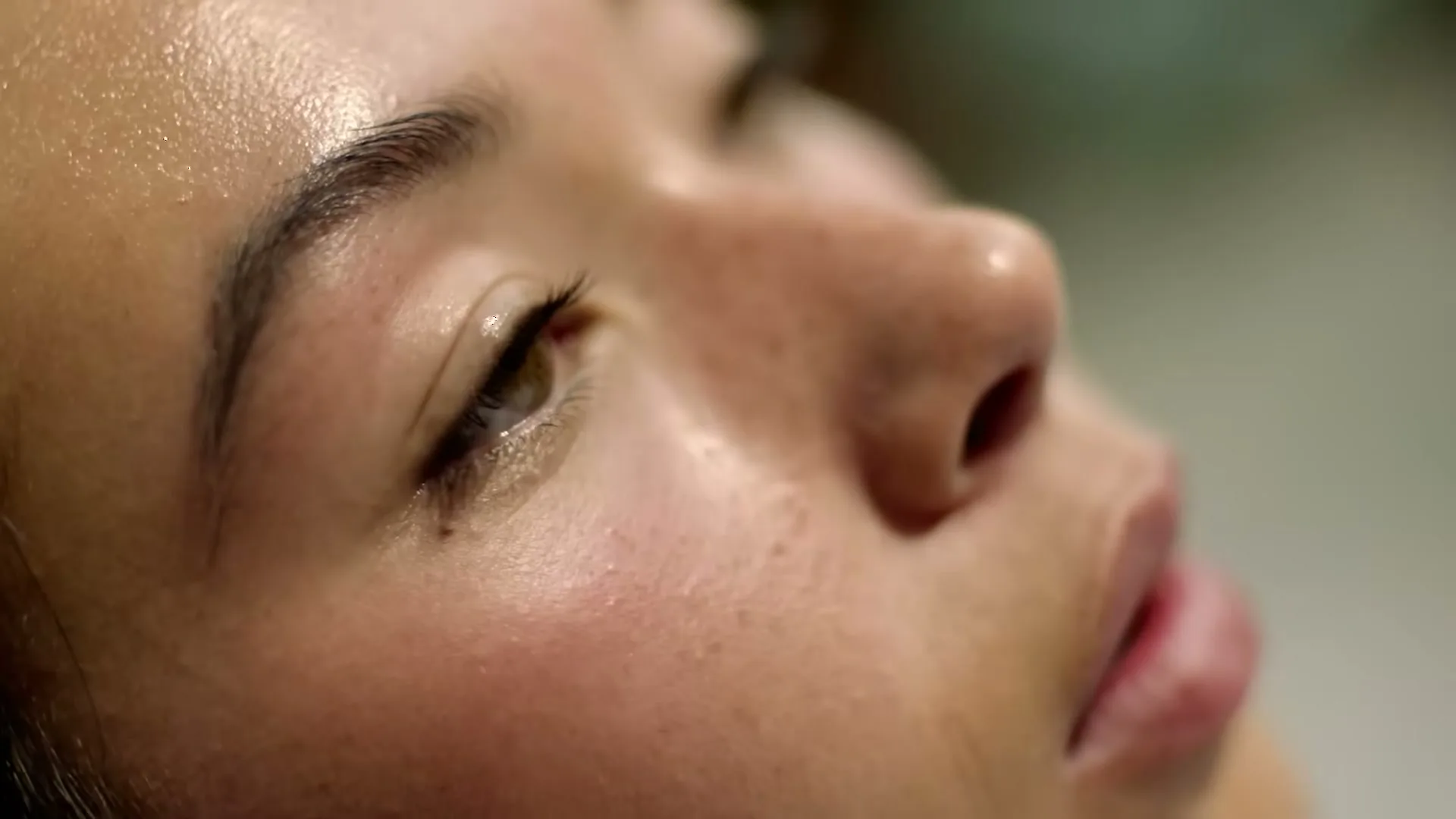 A woman's face, covered in sweat, is shown in an extreme closeup as her eye slowly opens, suggesting exertion or relaxation.