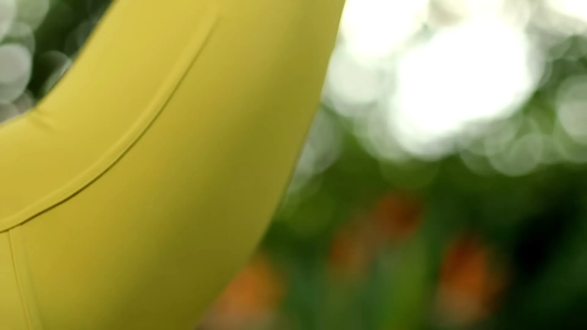 A person in a yellow top is seen in a closeup shot, with a blurred green and orange background, suggesting movement outdoors.