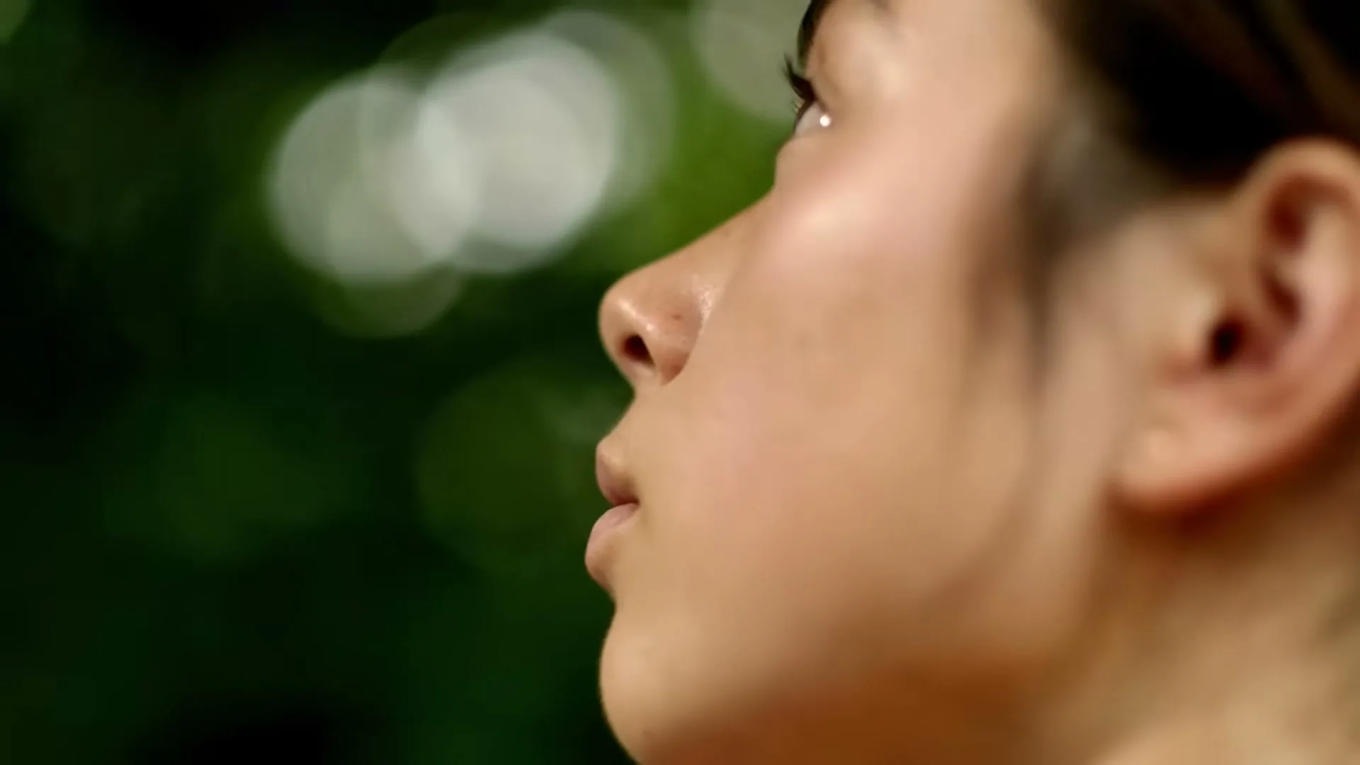 A young woman with her hair pulled back looks up with a serene expression, with "FEEL EMBRACE" text overlaid on a blurred green background.