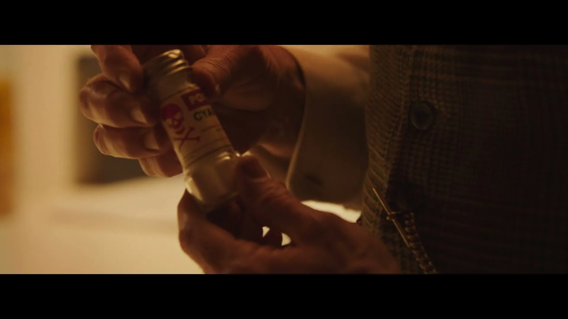 An older man's hands retrieve a small bottle labeled "POISON" with a skull and crossbones from his tweed waistcoat pocket.