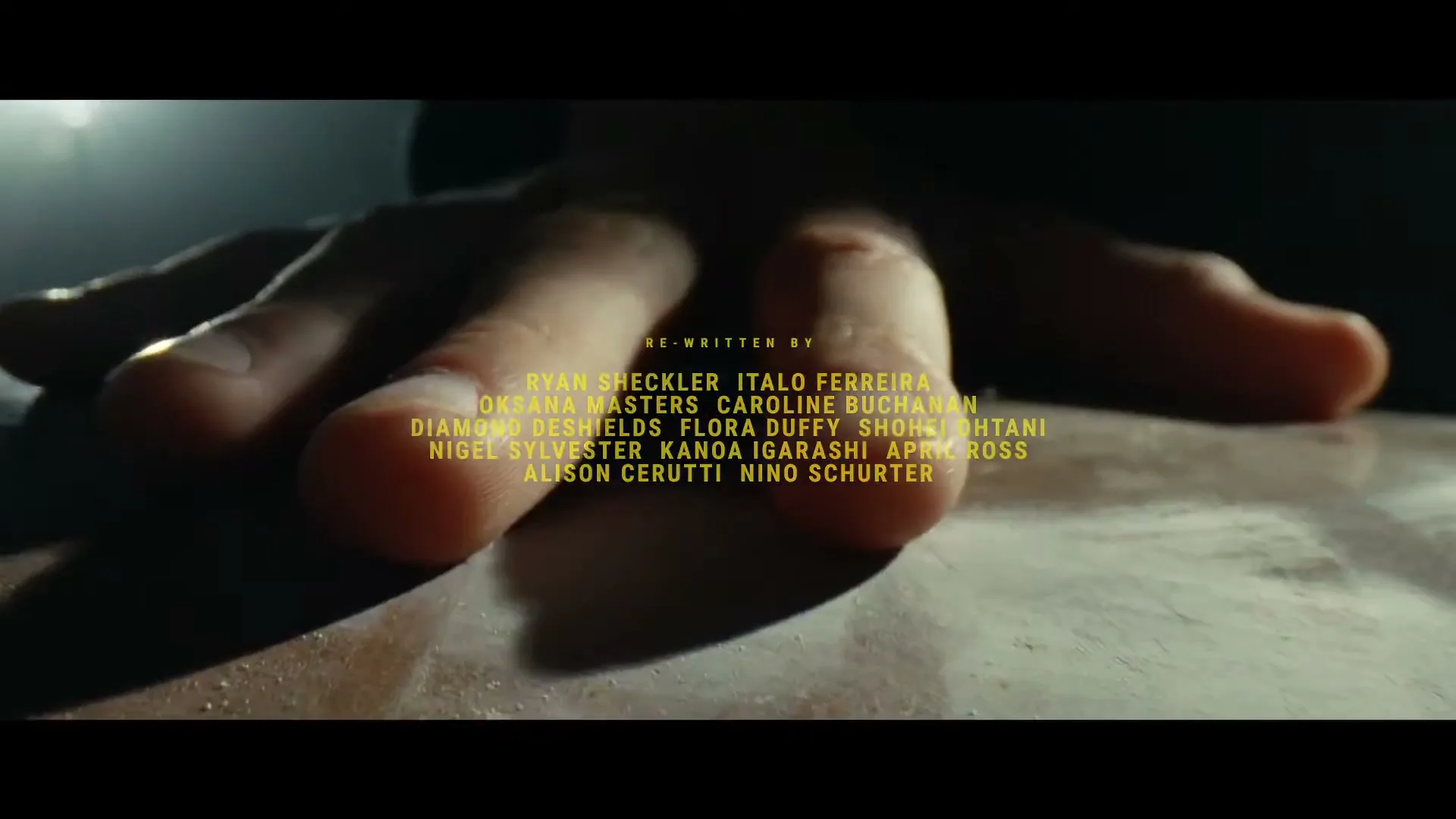 A person's hand is shown in a medium closeup, resting on a textured surface, with yellow text overlaid on the screen.