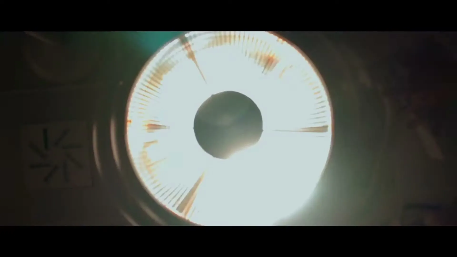 A bright, circular light source with a dark center is seen in a dark, industrial-looking interior, possibly a stadium or arena.
