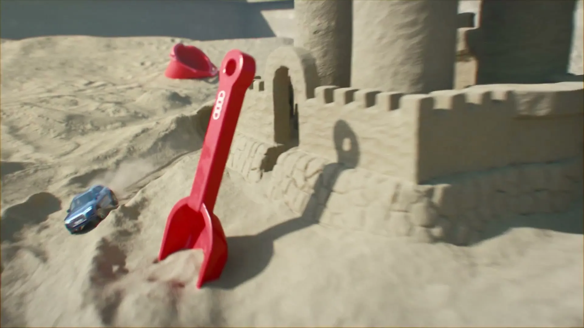 A toy Audi car emerges from a sand tunnel, drives around a sandcastle, and is joined by other toy cars and sand toys in a sandbox.
