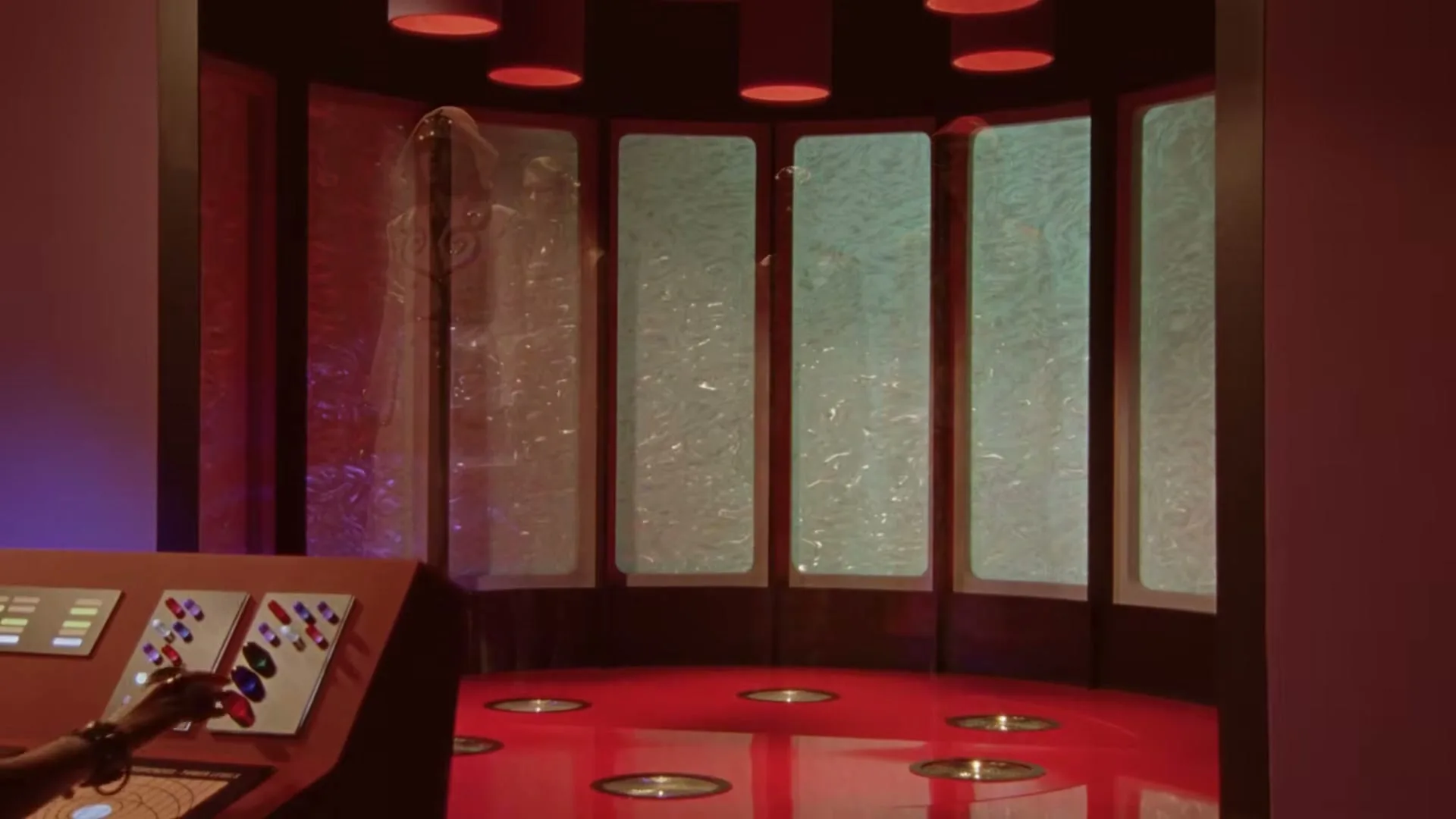 Four models in elaborate Gucci outfits materialize in a futuristic red room with a control panel, as a hand presses buttons.
