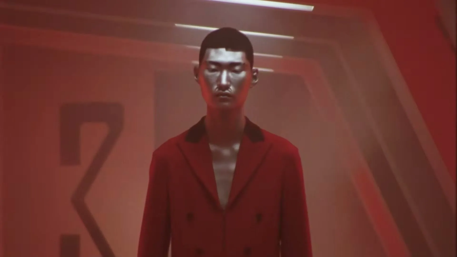 A male model with silver-painted skin and a red suit stands in a futuristic, dimly lit corridor, looking directly at the camera.