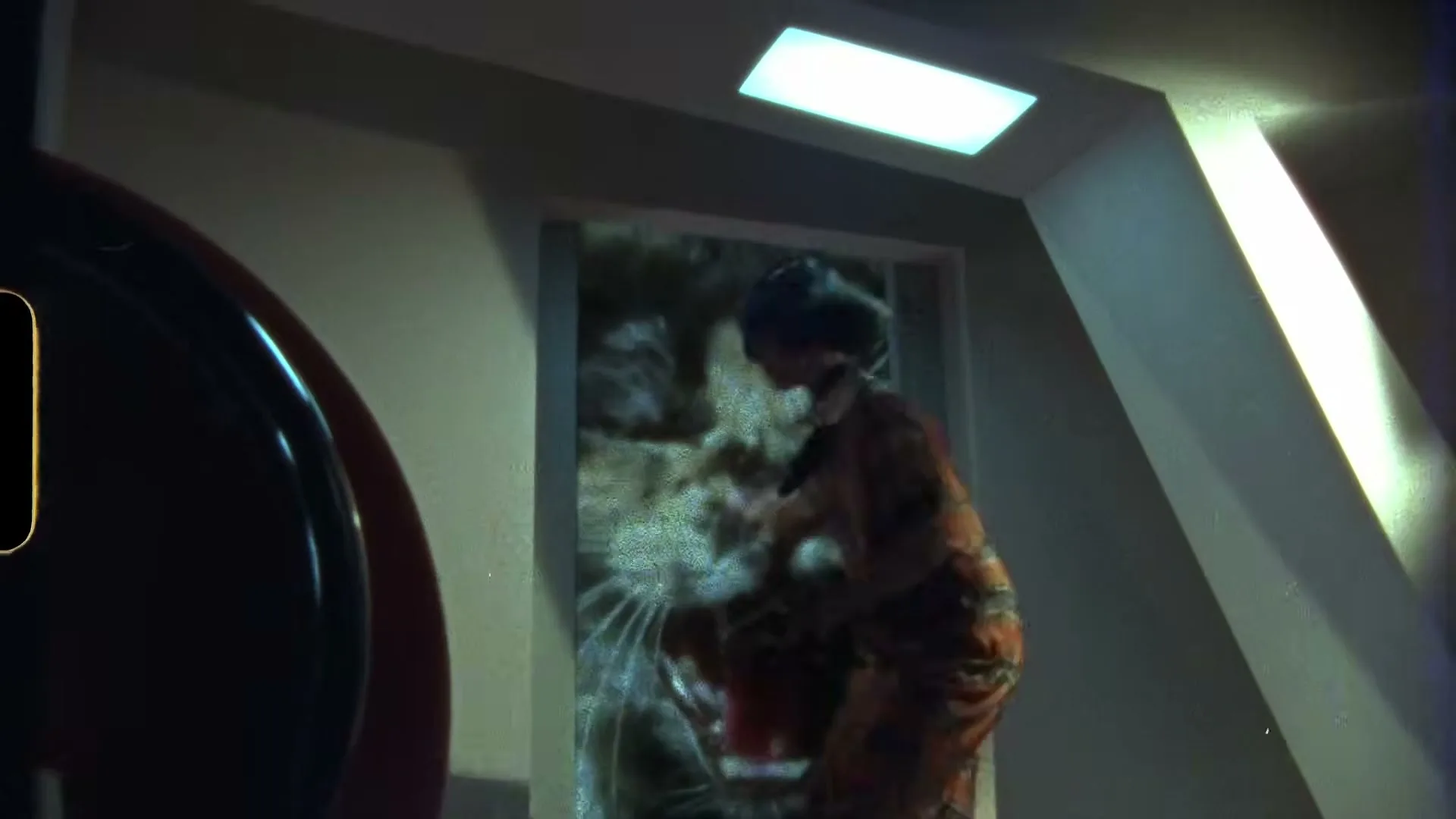 A woman in a retro-futuristic orange jumpsuit and helmet walks towards a door, which reveals a giant cat's face as she opens it in a spaceship interior.