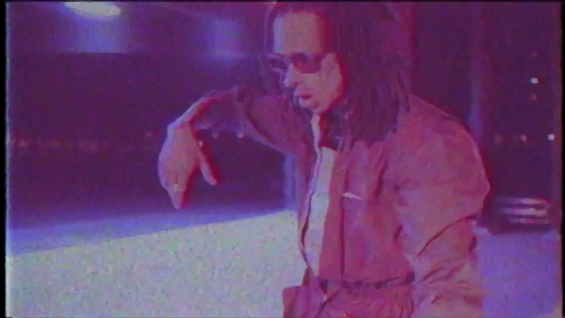 A man with dreadlocks and sunglasses dances in a dark, neon-lit space, captured with a glitchy, VHS aesthetic.