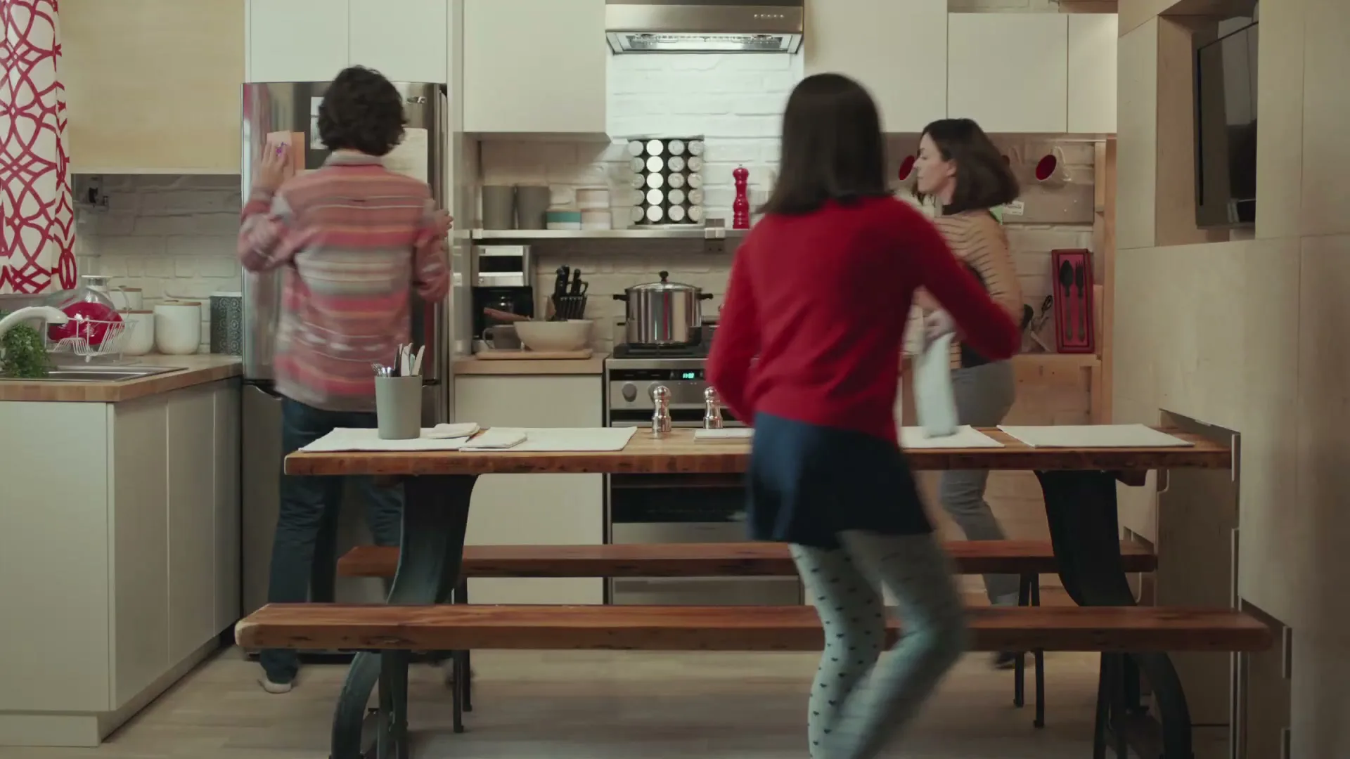 A family of four, including a father, mother, son, and daughter, are seen moving around a modern kitchen, preparing food and drinks.