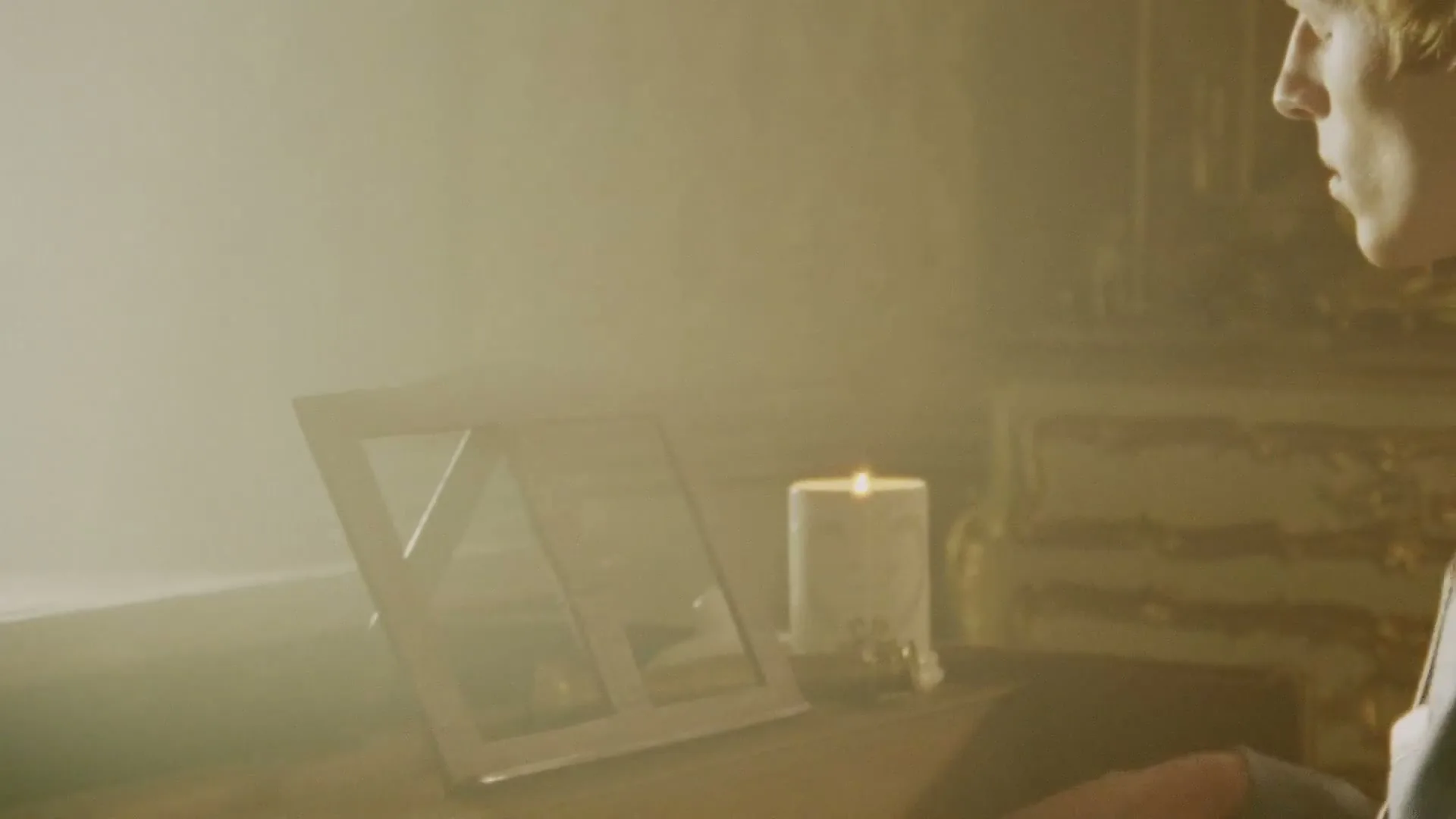 A young man with blonde hair sits at a piano, playing a melancholic tune in a dimly lit, ornate room.
