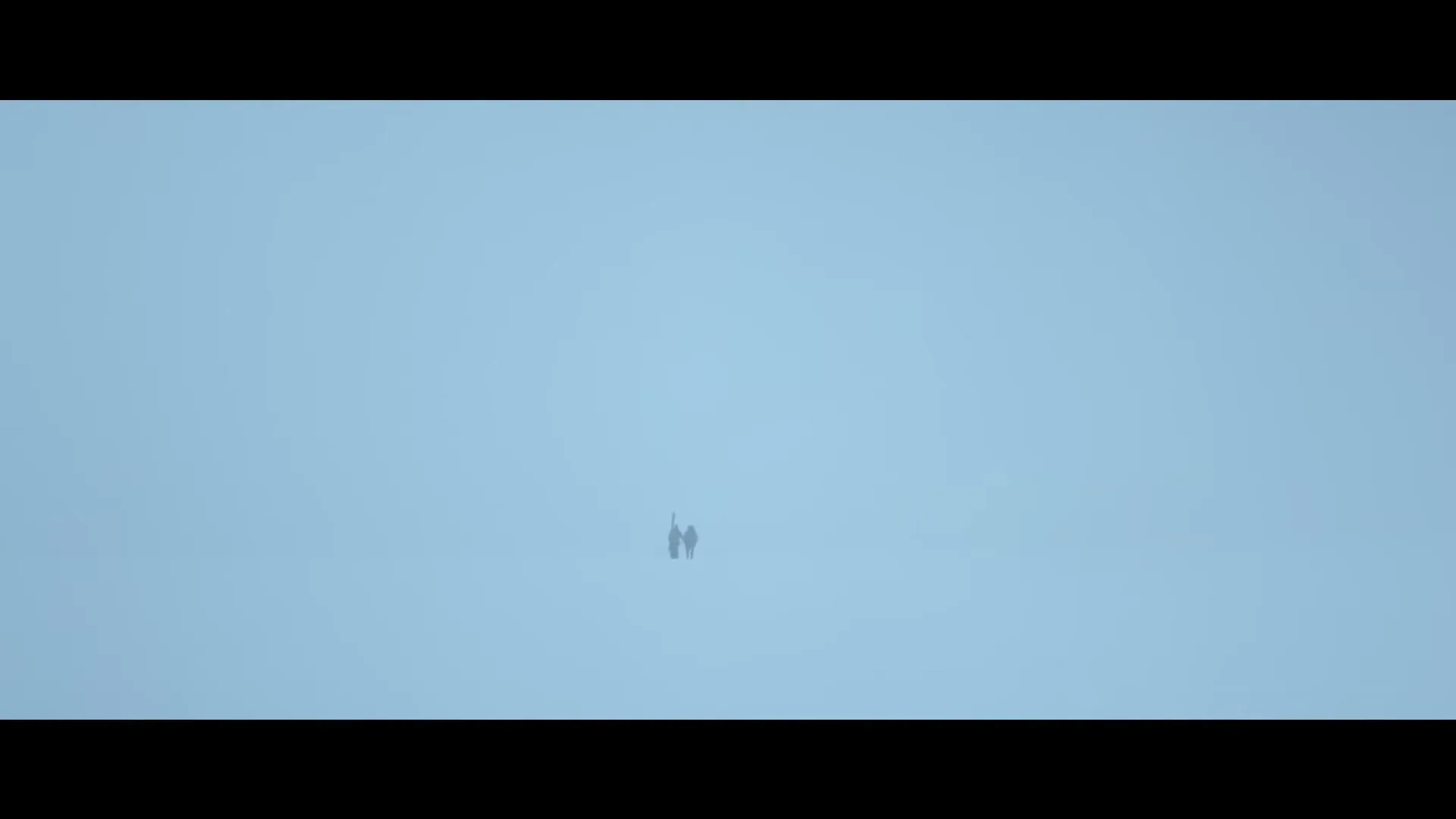 A wide shot of a person on skis being pulled by a horse through a snowy, foggy landscape, with mountains in the background.