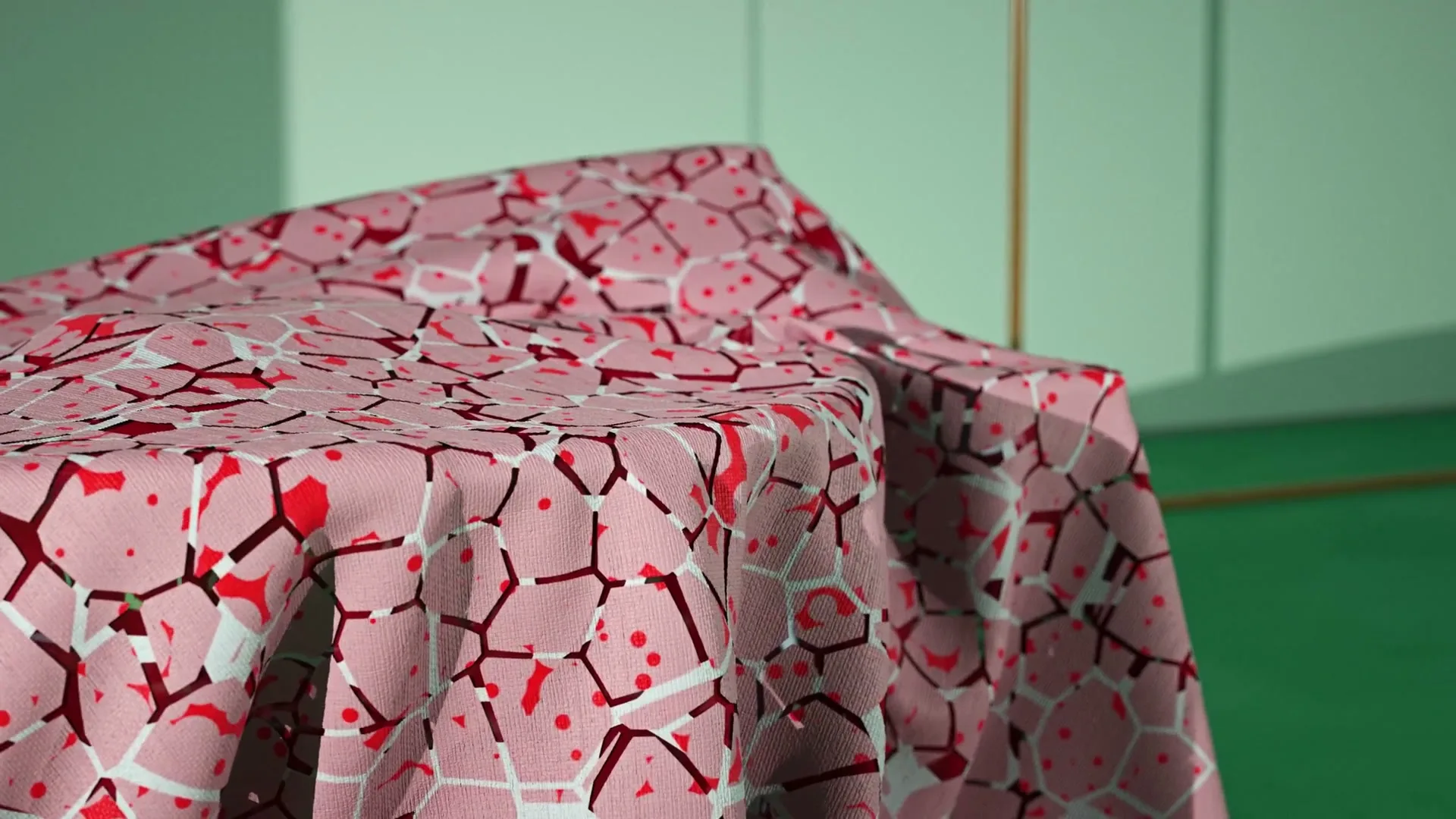 A pink tablecloth with a red and white geometric pattern is draped over an unseen object in a room with green walls.