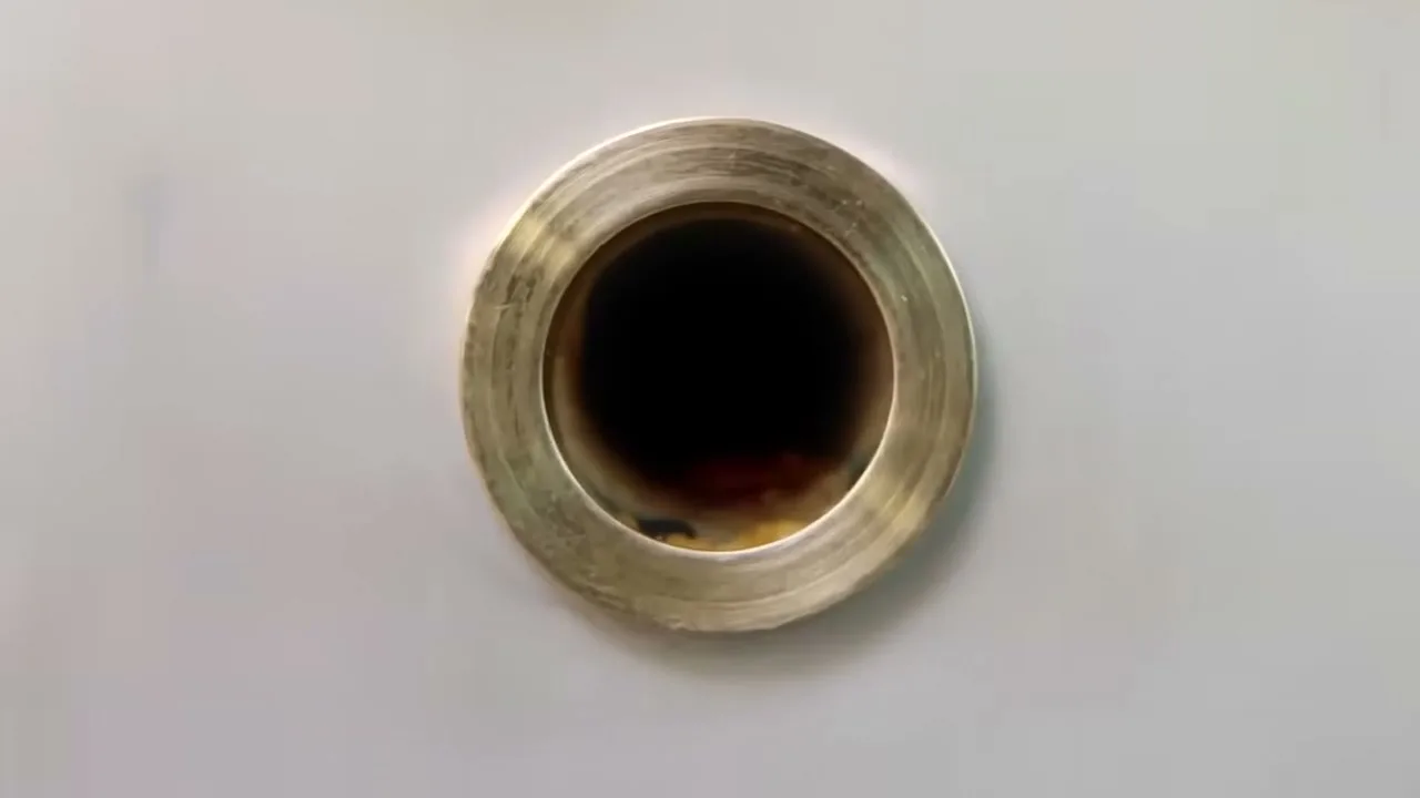 A close-up shot of a brass-colored circular opening on a white surface, with a dark interior, suggesting a peephole or small tunnel.