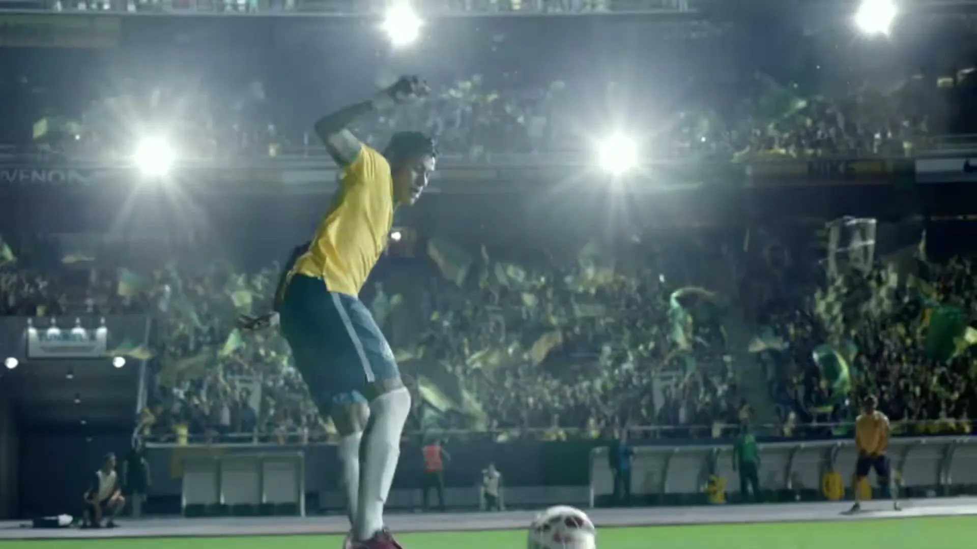 Neymar Jr. in a yellow and blue uniform, jumps to kick a soccer ball in a stadium full of cheering fans at night.
