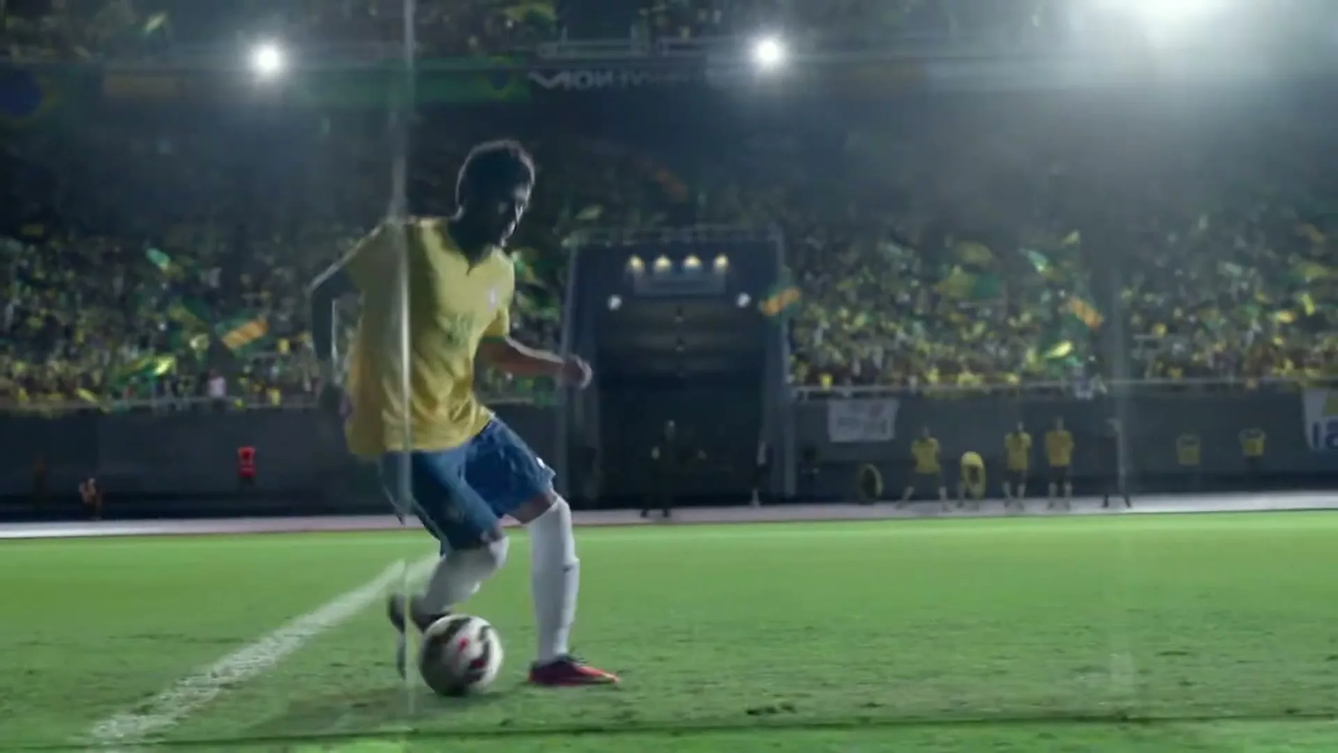 Neymar Jr. in a yellow and blue uniform dribbles a soccer ball on a green field in a stadium at night, with a defender sliding in.
