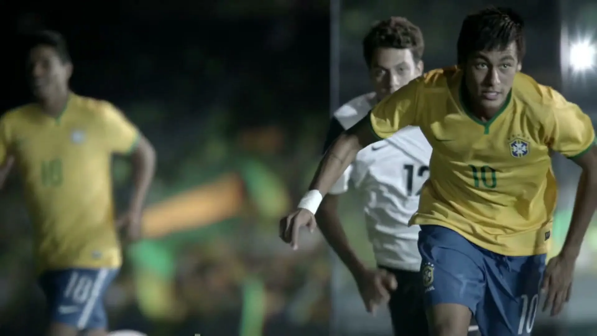 Neymar Jr. in a yellow and blue soccer uniform runs on a field with other players, looking intensely at the camera.