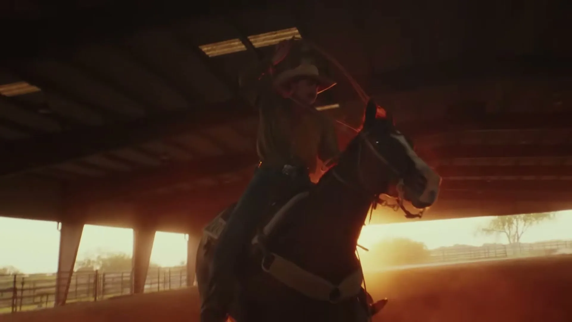 A cowboy on horseback, wearing a hat and western attire, practices roping in a dusty arena at sunset.