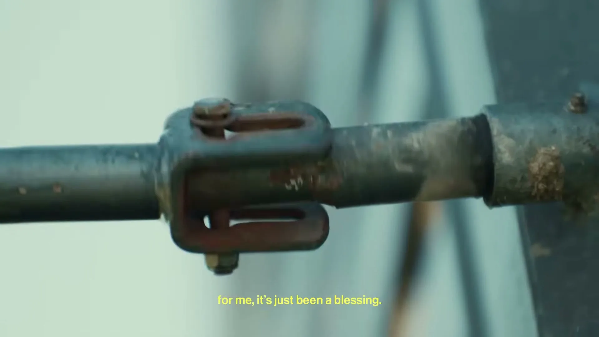 A close-up shot of a rusty metal rod with a U-shaped bracket, possibly part of a vehicle, with a subtitle at the bottom.