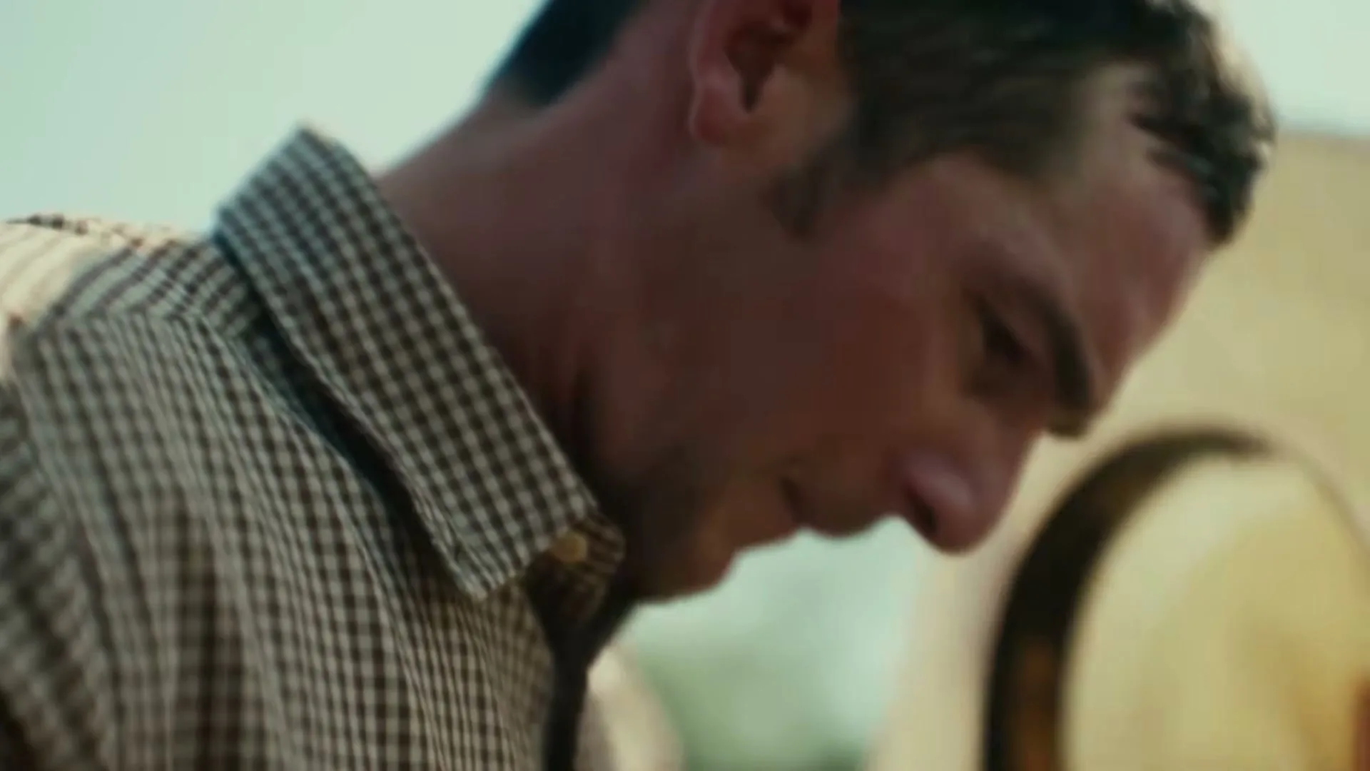 A man in a plaid shirt wipes his face with a colorful cloth, then puts on a cowboy hat, outdoors.