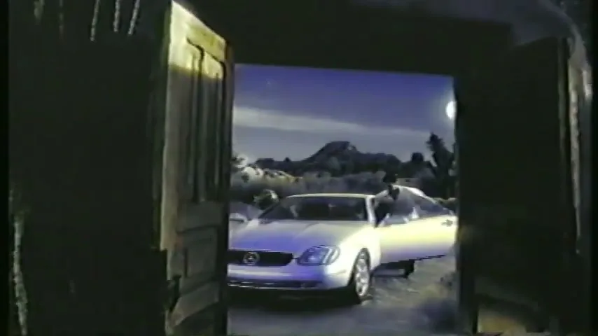 A man in a white shirt gets into a silver Mercedes-Benz convertible, which is parked in a desert landscape under a starry night sky with a full moon.